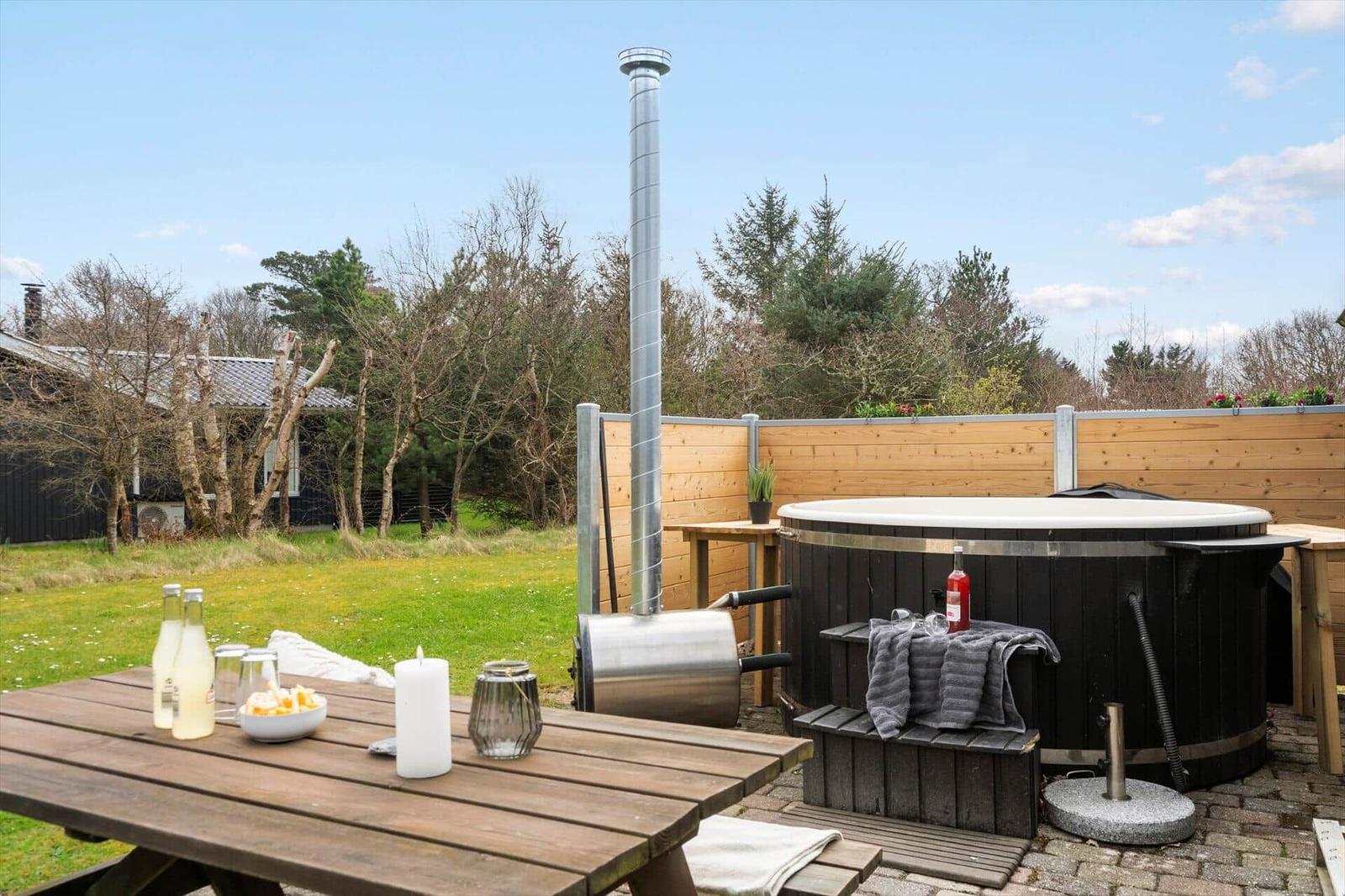 Außenbereich mit Whirlpool, Grill und Tisch. Hintergrund: Holzzaun und Wald.