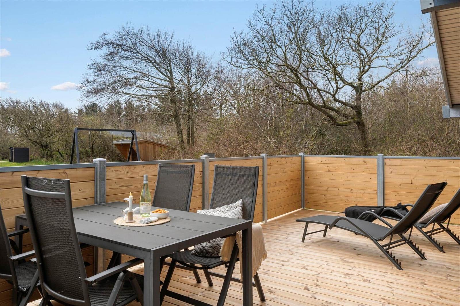 Terrasse mit Tisch, Stühlen und Liegen. Holzgeländer und Bäume im Hintergrund.