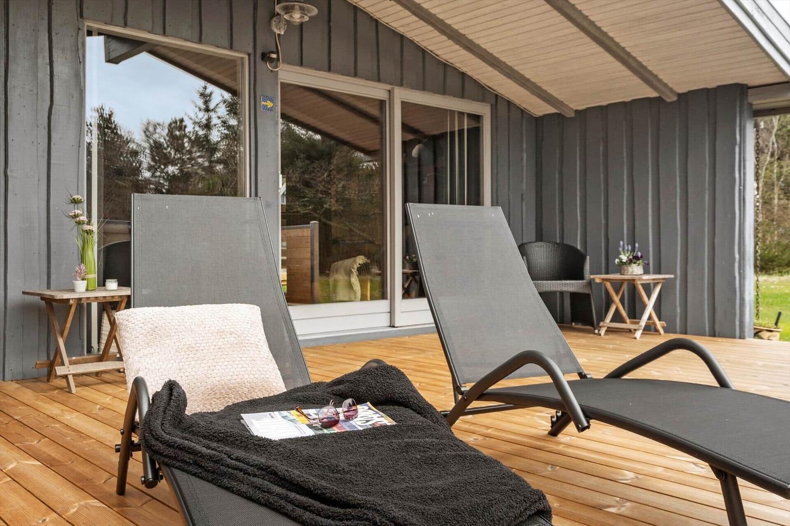 Terrasse mit zwei Liegestühlen, Holzdielen und Glasfront zur Unterkunft.