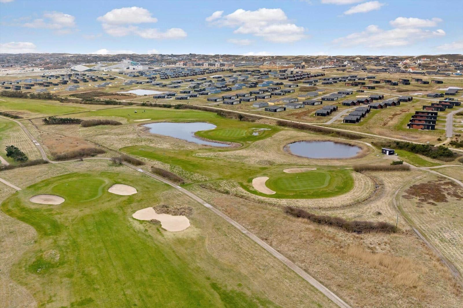 Golfplatz mit Bächen und Sandbunkern. Hintergrund: Ferienhäuser und Landschaft.