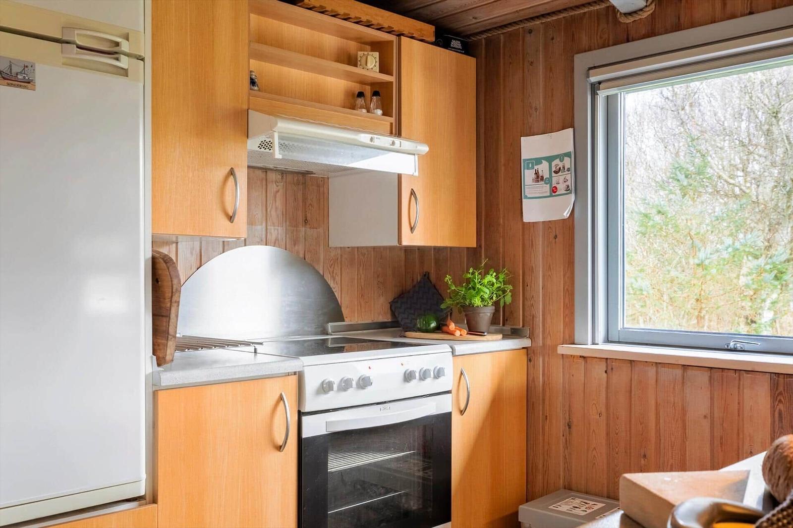 Küche mit Holzschränken, Kühlschrank, Herd und Fenster mit Blick auf Wald.