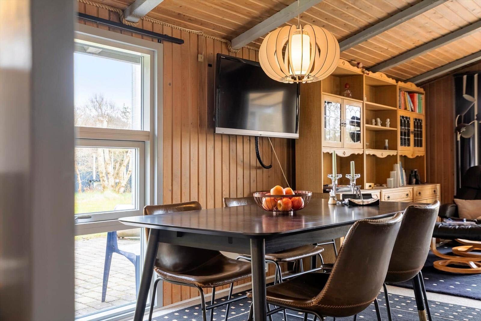 Esszimmer mit Holzwand, Tisch, Stühlen und Fernseher an der Wand.