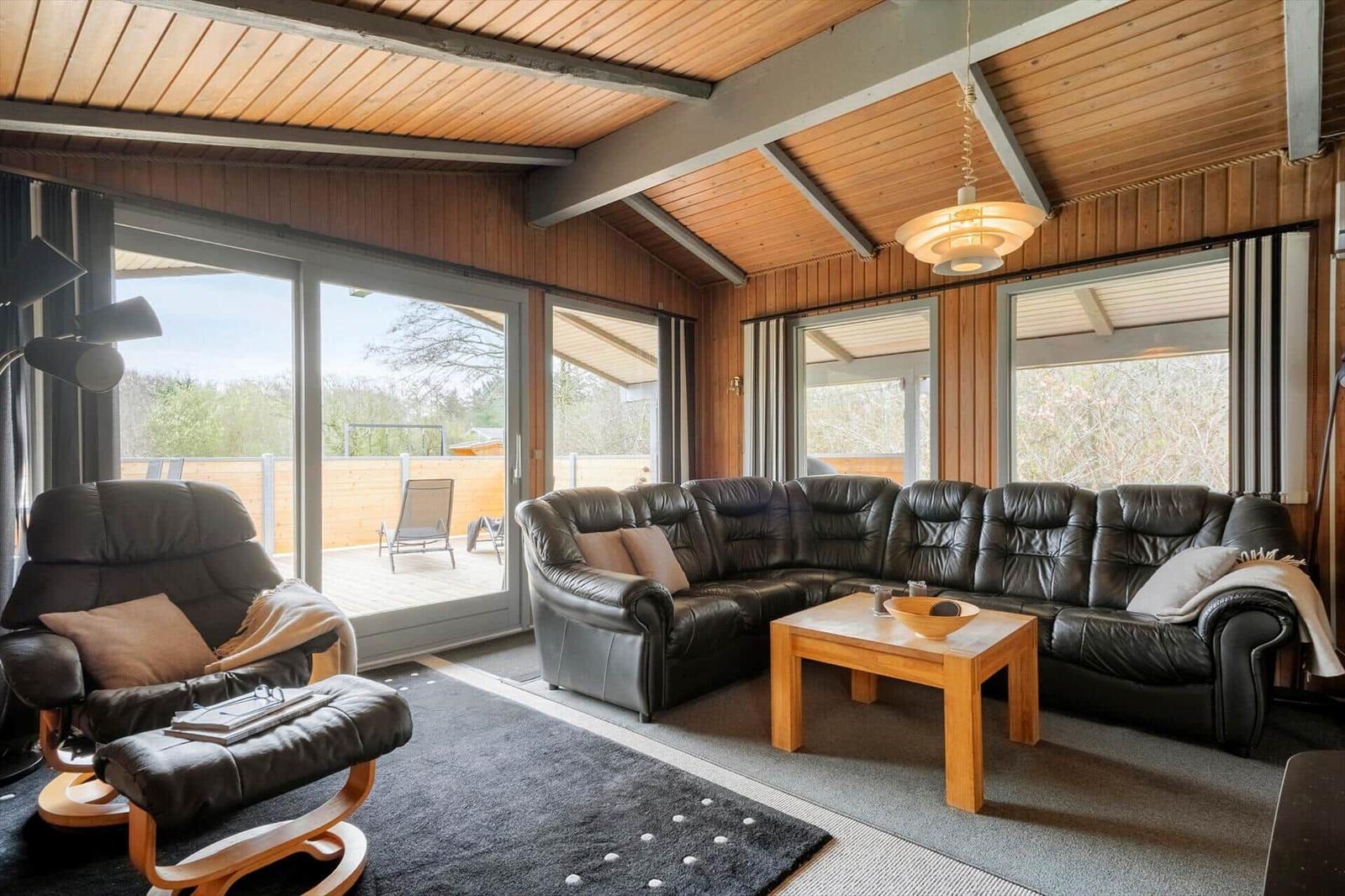 Wohnzimmer mit Leder-Sofa, Sessel und Holztisch. Große Fenster und Terrasse.