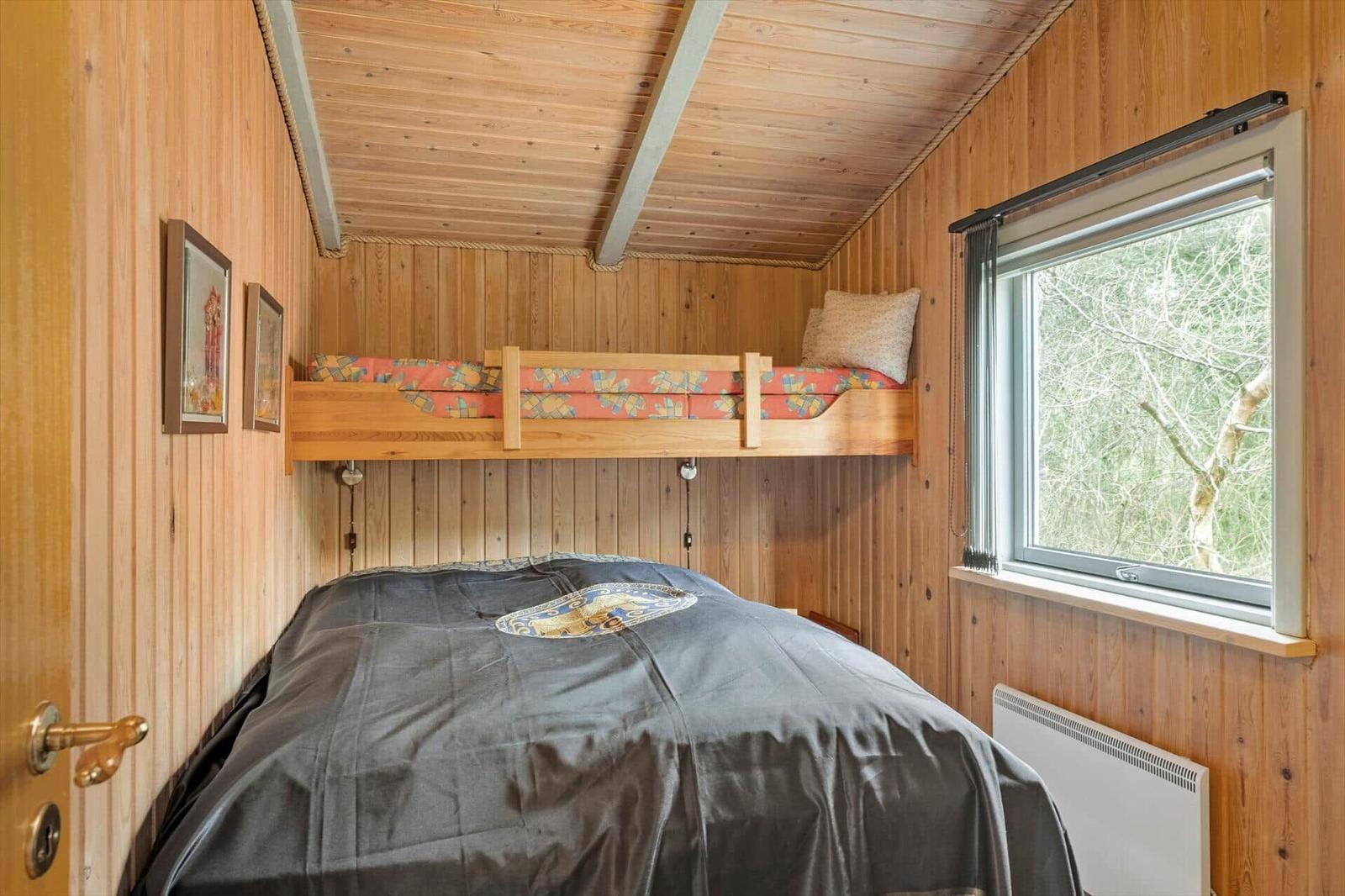 Zimmer mit Doppelbett und erhöhtem Bett, Holzwand und Fenster mit Waldblick.