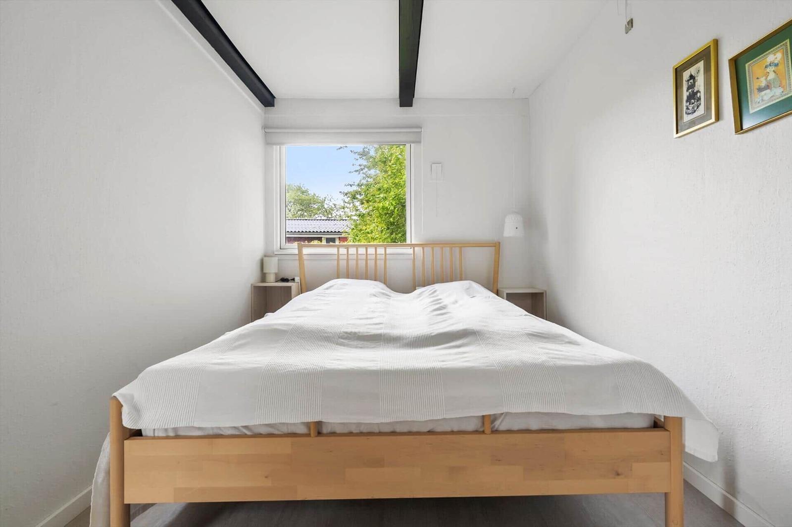 A bedroom with a bed, two nightstands, and a window with a view of trees.