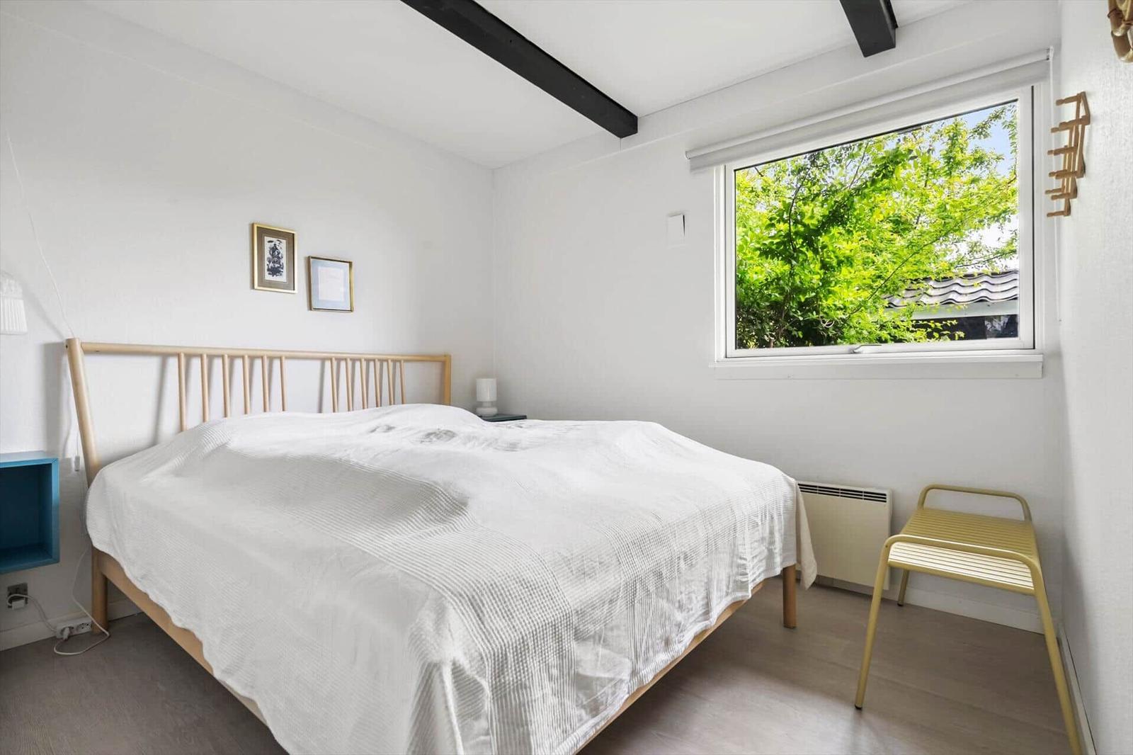 Bedroom with bed, window, and chair. Ceiling beams and wall pictures are visible.