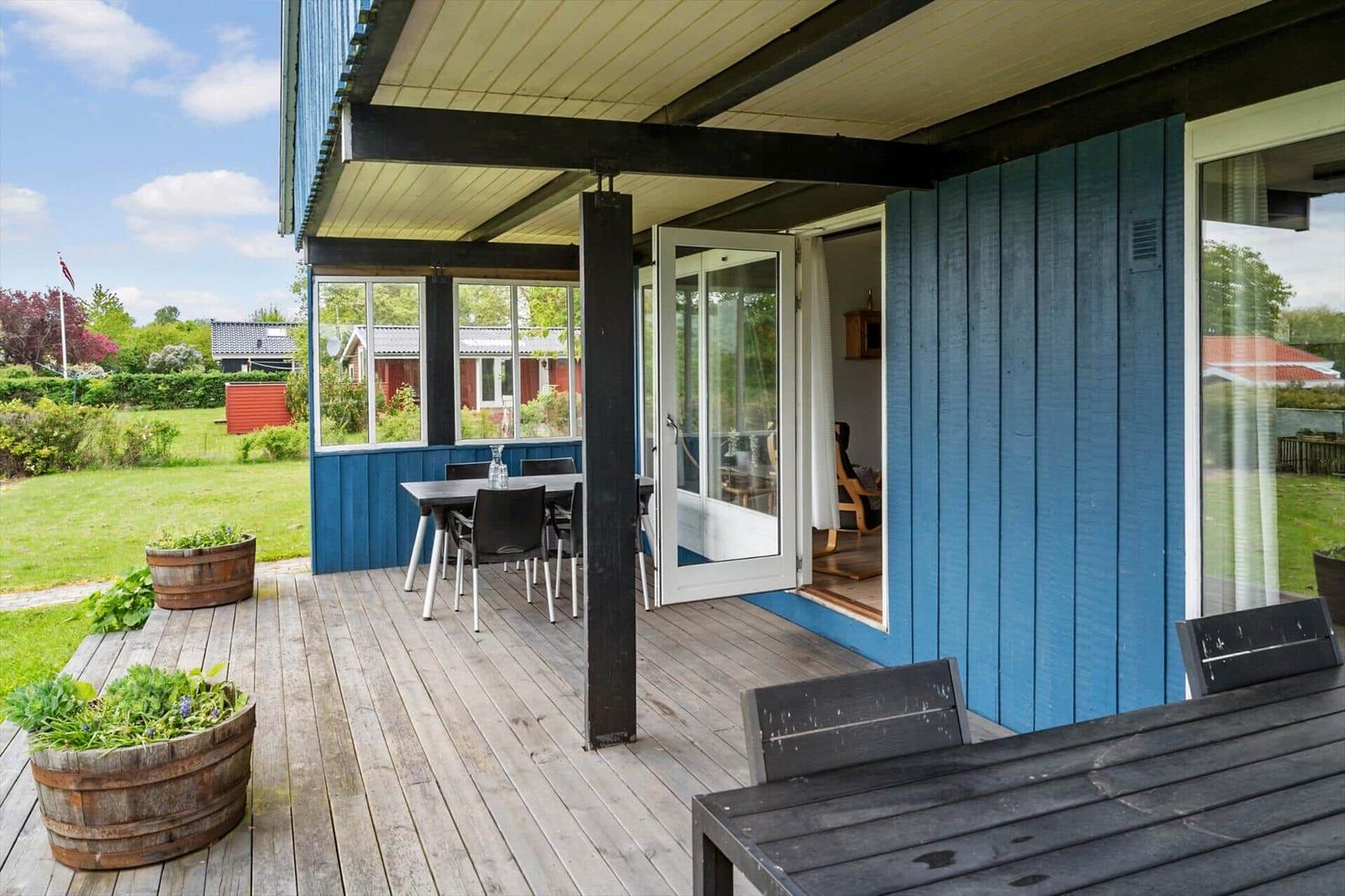 Terrace with table, chairs, and wooden barrels. Glass doors lead into the house.