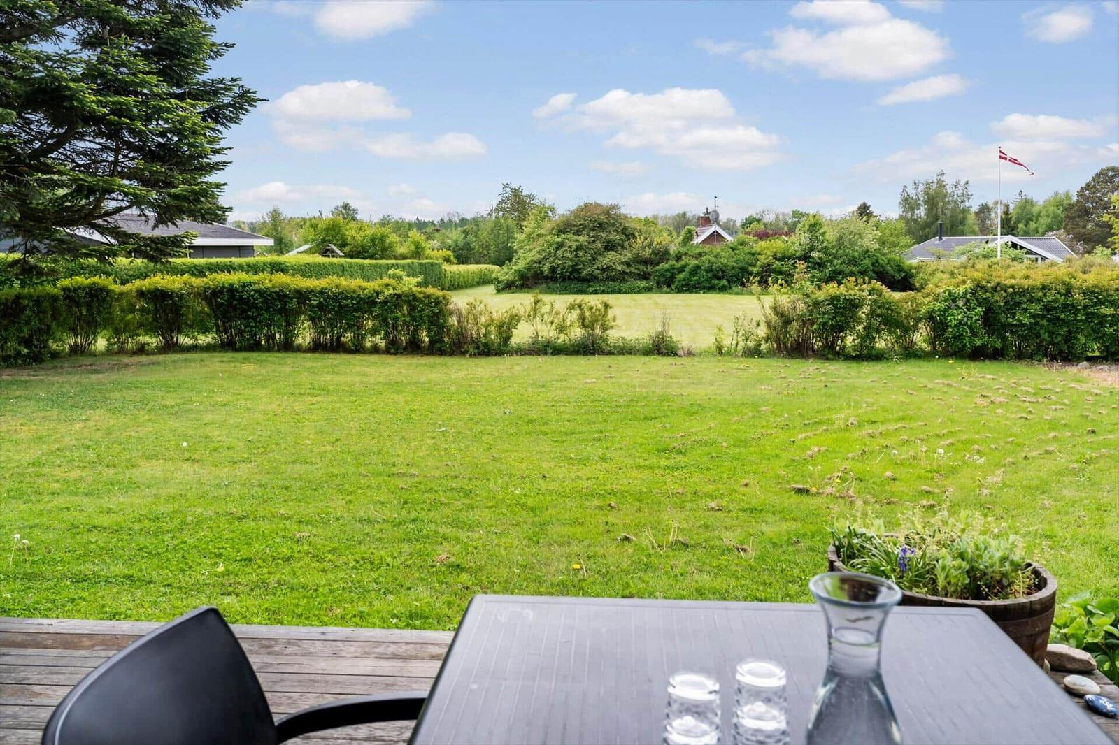 Large green garden with terrace and table. Trees and houses are visible in the background.