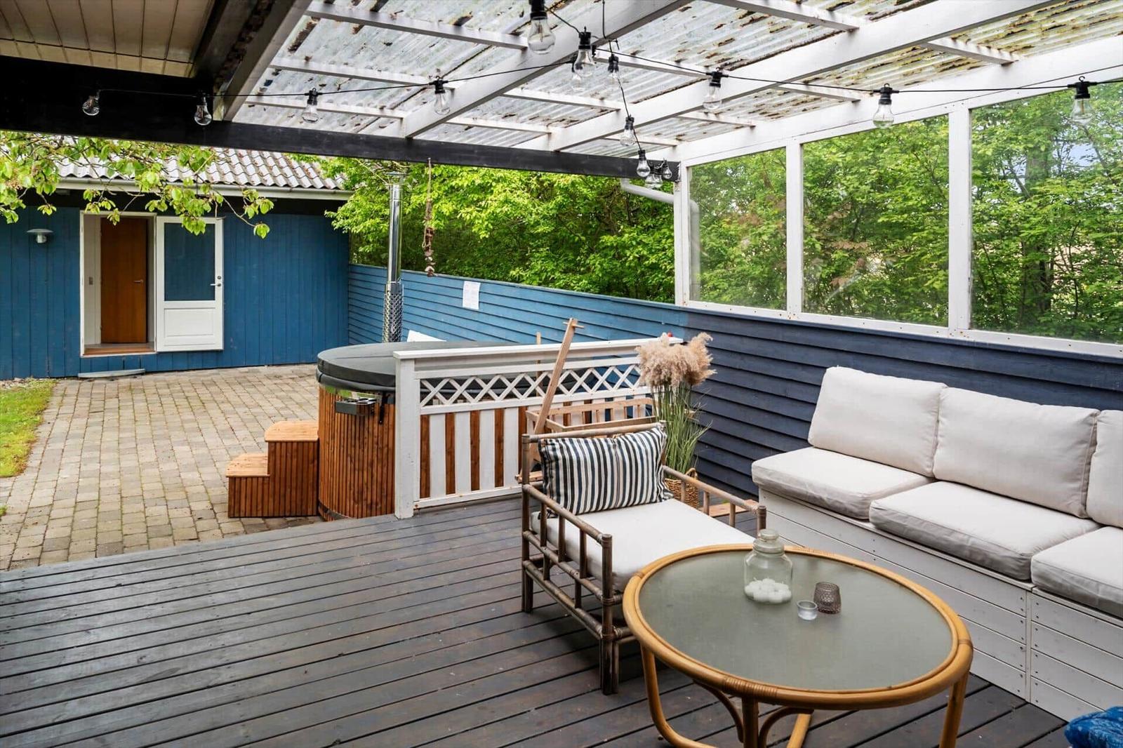 Deck with seating, table, and hot tub under roof with string lights.