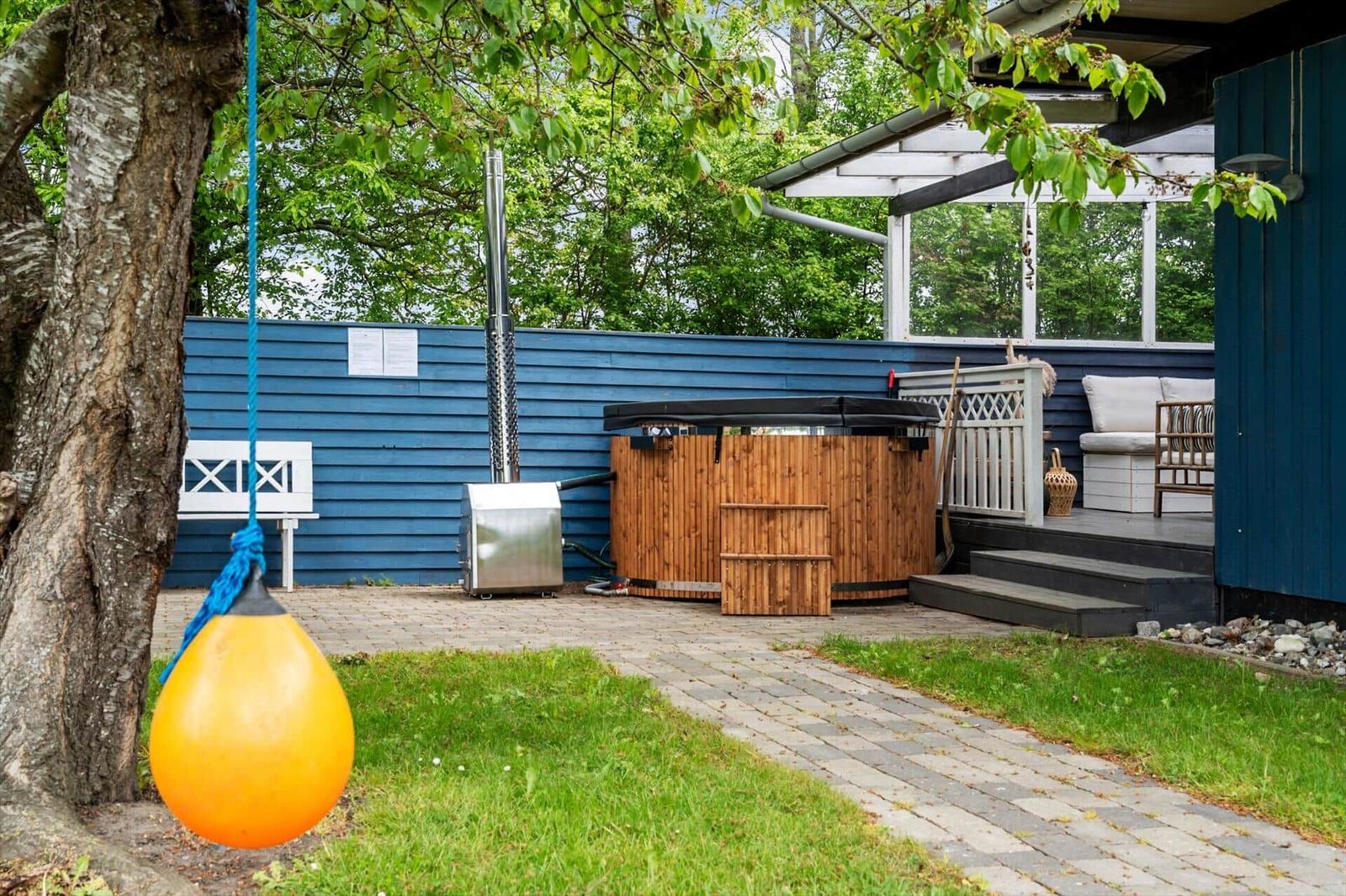 Backyard with wooden hot tub, terrace, and orange buoy hanging from tree.