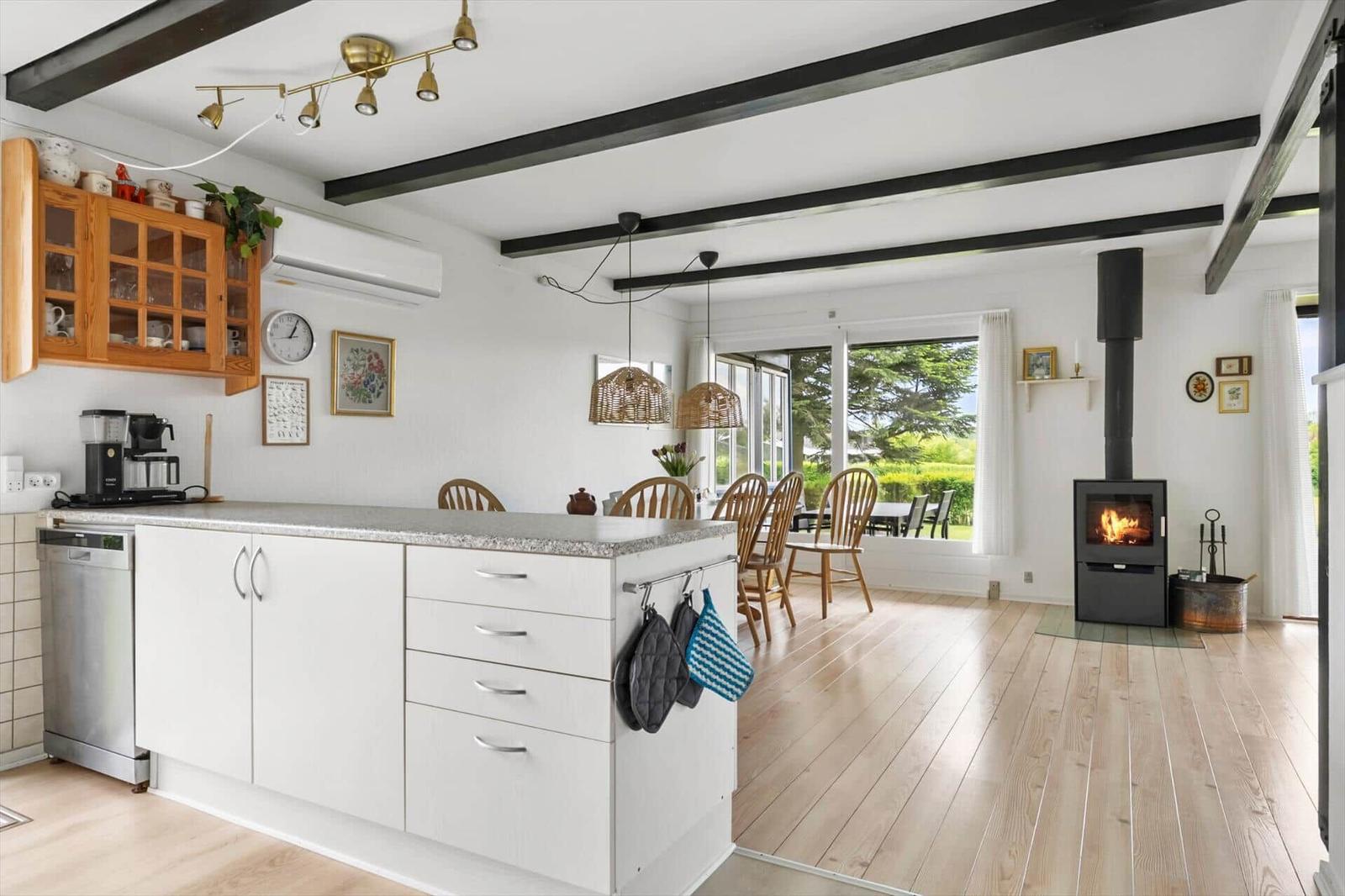 Kitchen with dining area and wood-burning stove. Wooden floor and black beams on ceiling.