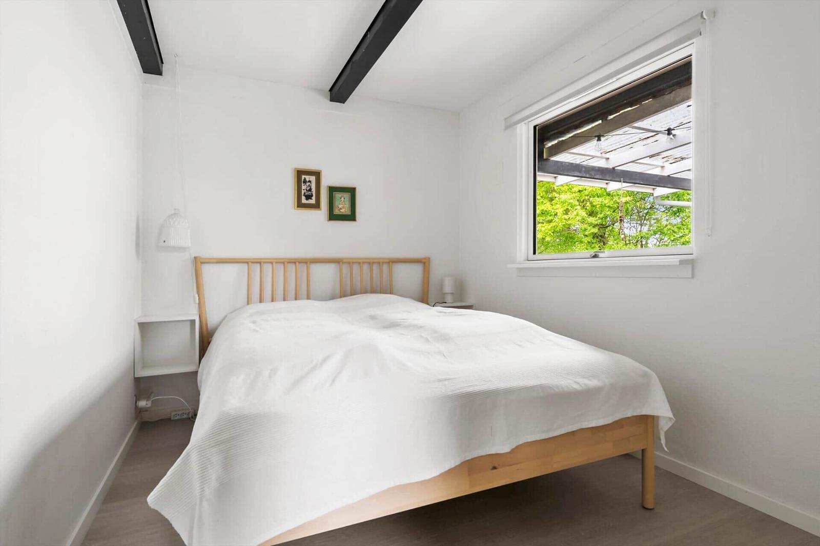 Bedroom with wooden bed, window, and white walls.