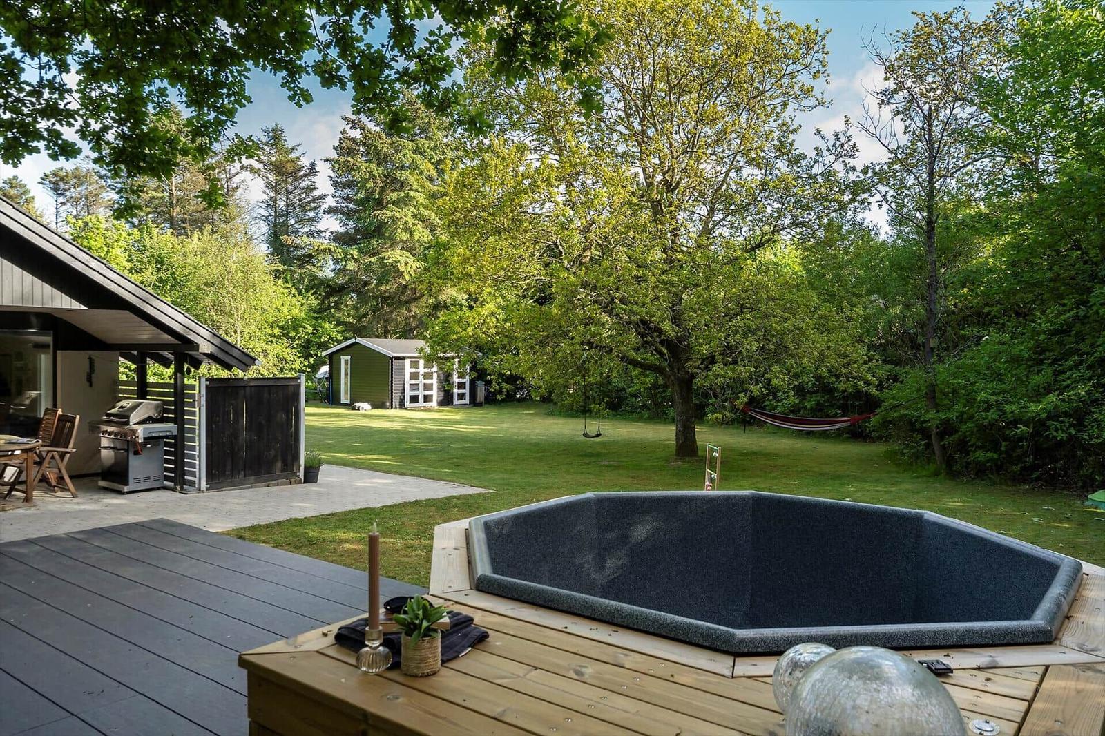 Hütte mit Whirlpool, Grill und Grünfläche im Wald.