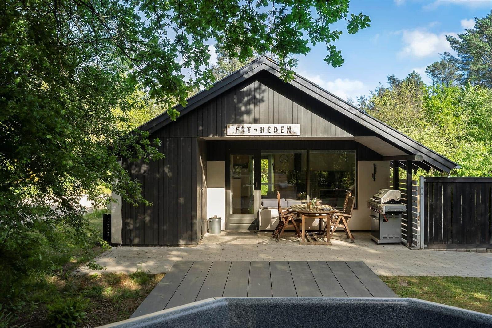 Holzhaus mit Terrasse, Grill und Sitzgelegenheit unter Bäumen.