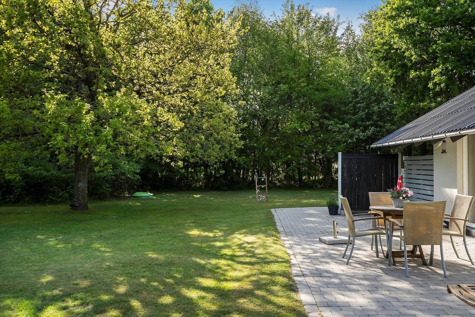 Garten mit Rasenfläche, Terrasse und Sitzgruppe unter Bäumen.