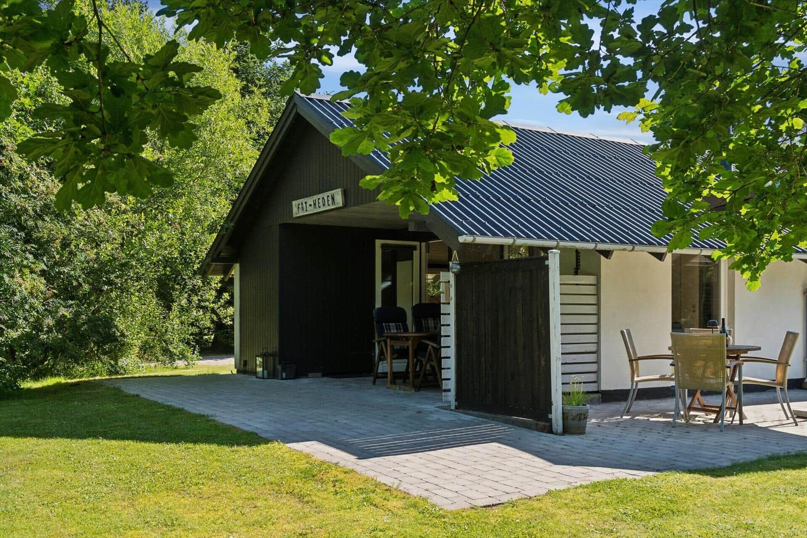 Haus mit Terrasse, Garten und Tisch mit Stühlen unter Bäumen.