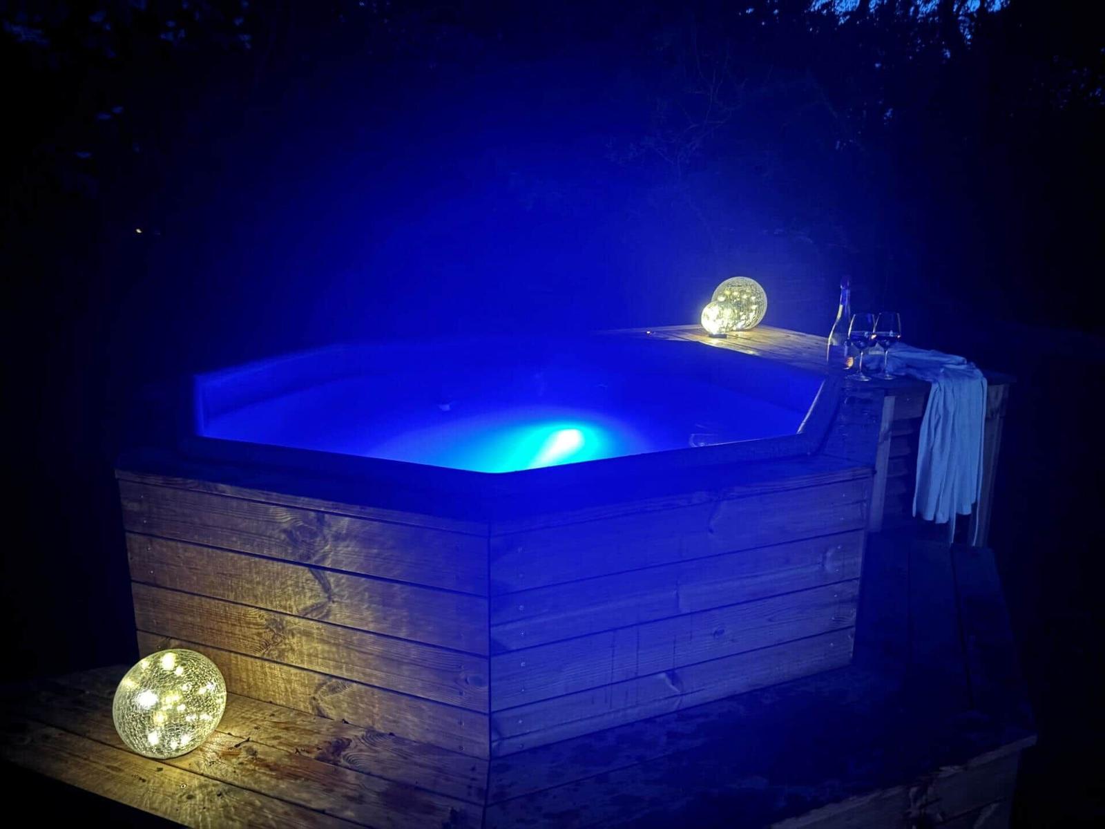 Ein Außenwhirlpool mit blauer Beleuchtung, umgeben von Holz und Glühbirnen.