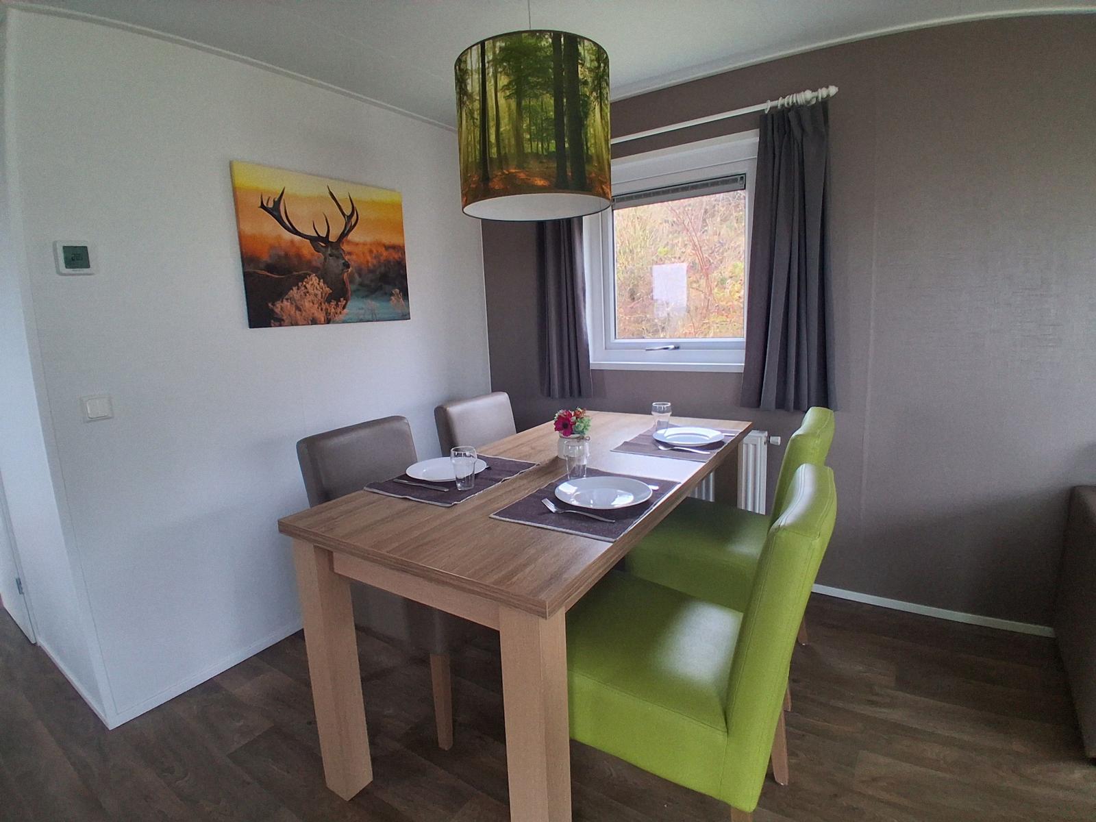 Esstisch mit vier Stühlen, Wandbild und Fenster mit Vorhängen.