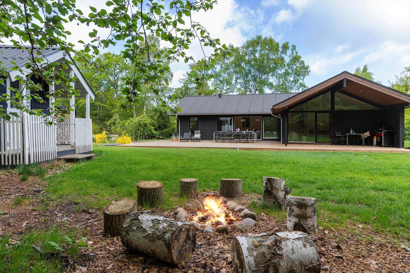Haus mit Grillplatz und Feuerstelle im Garten. Holzstapel um Feuer. Terrasse mit Sitzgelegenheit.