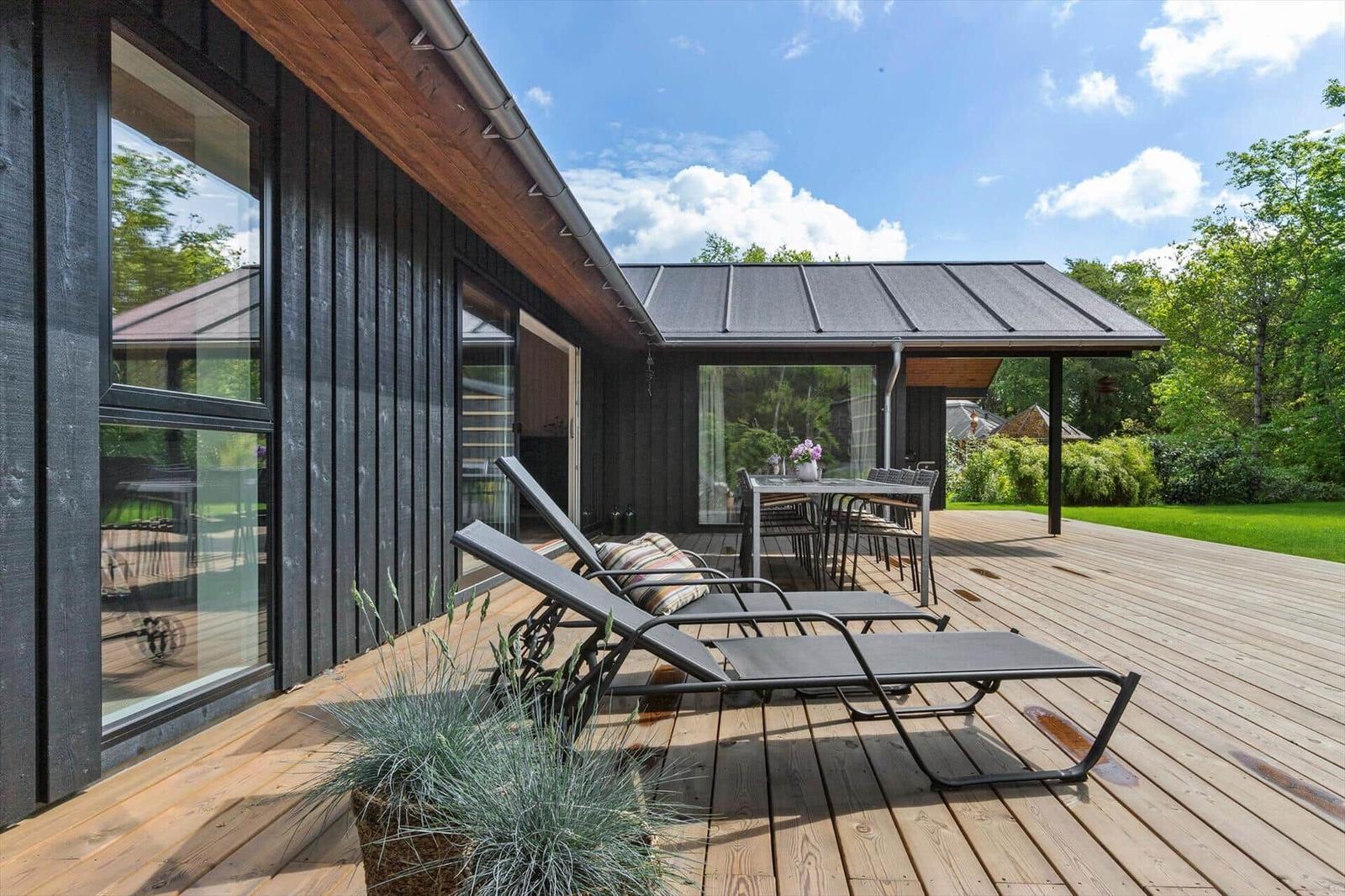 Terrasse mit Liegestühlen und Tisch unter einem Dach. Holzdecke, grüne Umgebung.