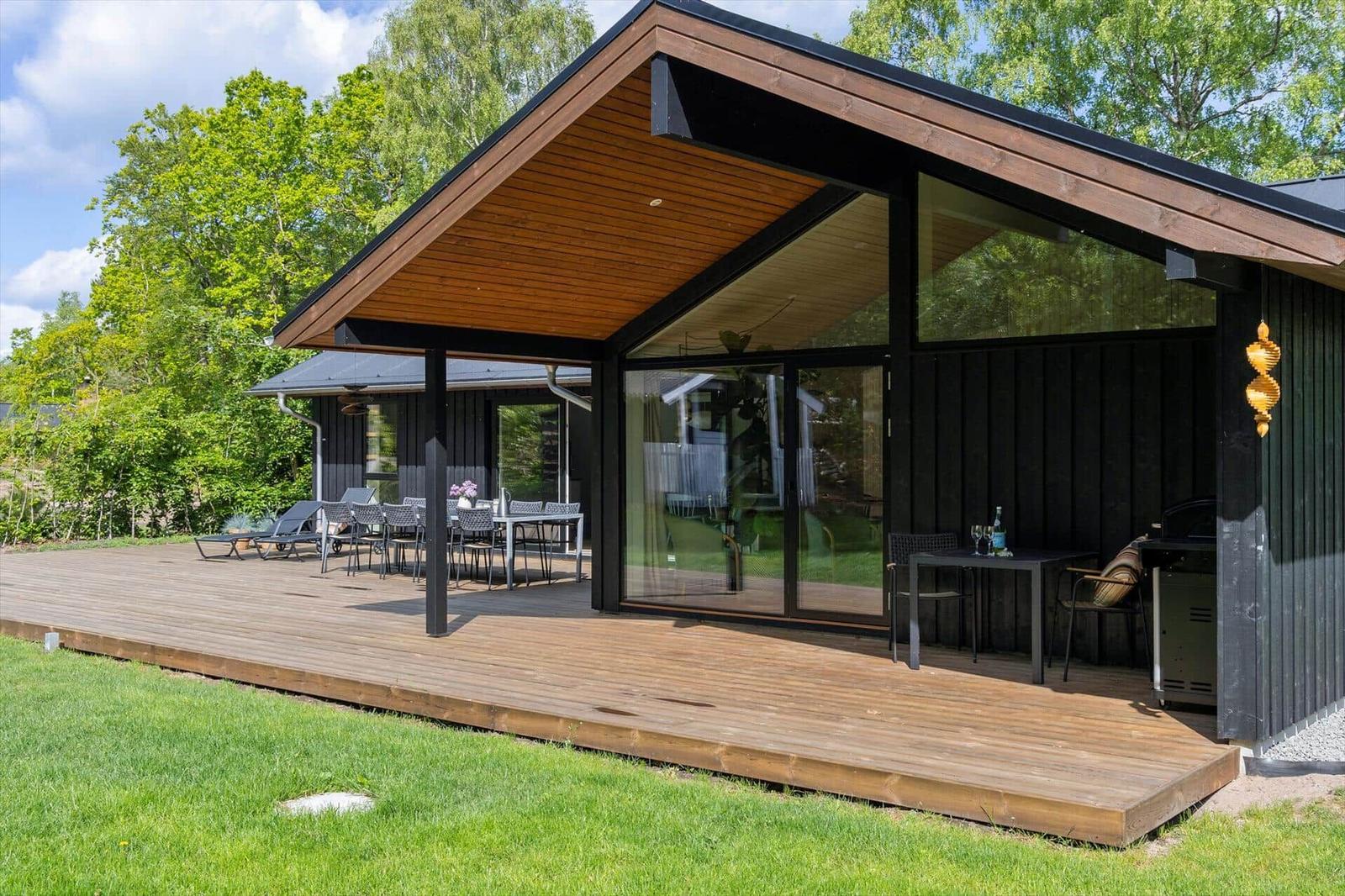 Moderne Villa mit Holzterrasse, Sitzgelegenheiten und Grillbereich im Grünen.