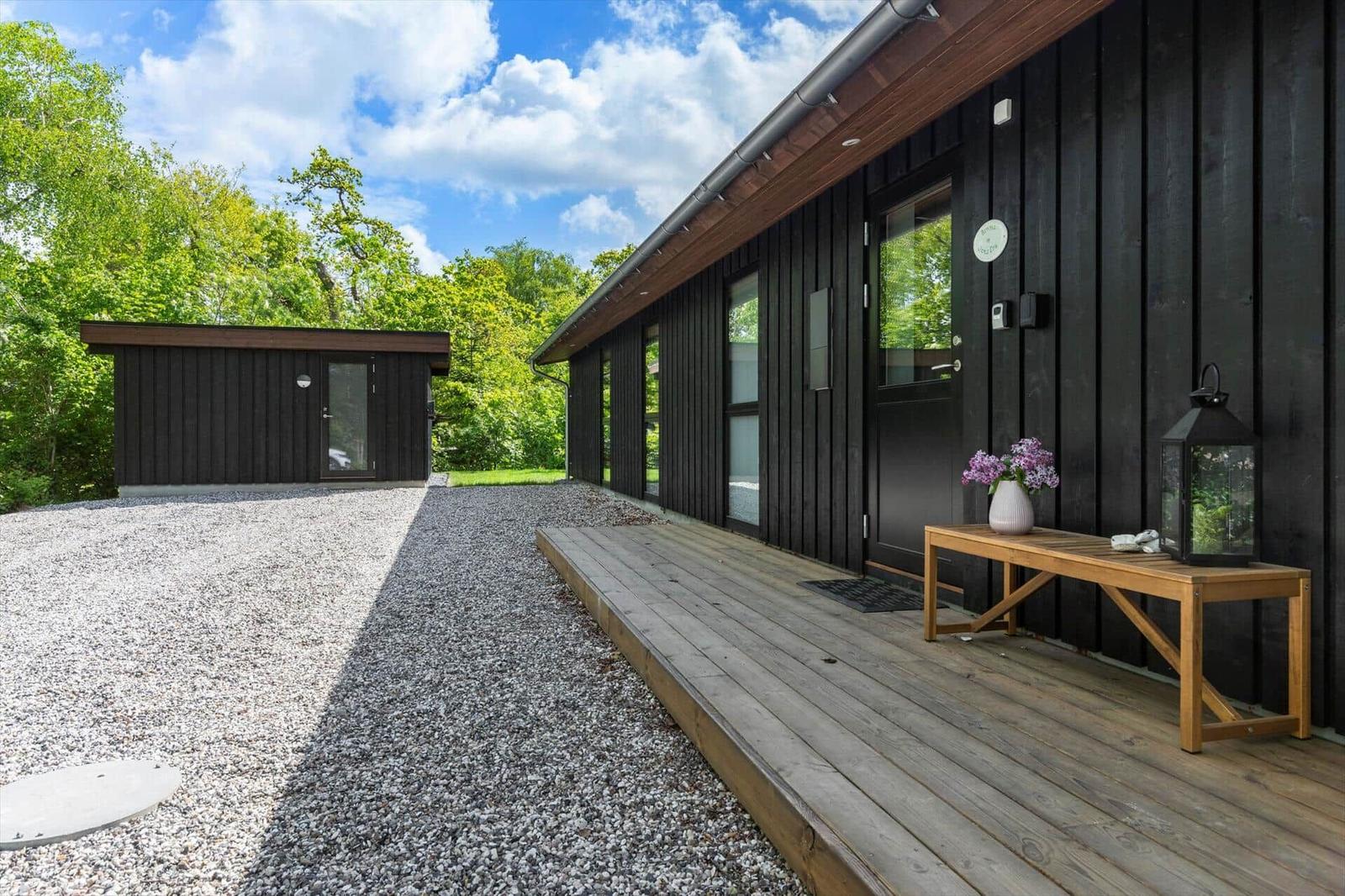 Moderne Holzhütte mit Holzterrasse und Blumen. Hinterhof mit Gras und Bäumen.