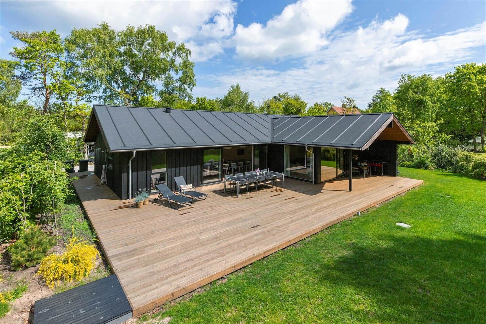 Moderne Villa mit Holzterrasse, Garten und großem Essbereich im Freien.
