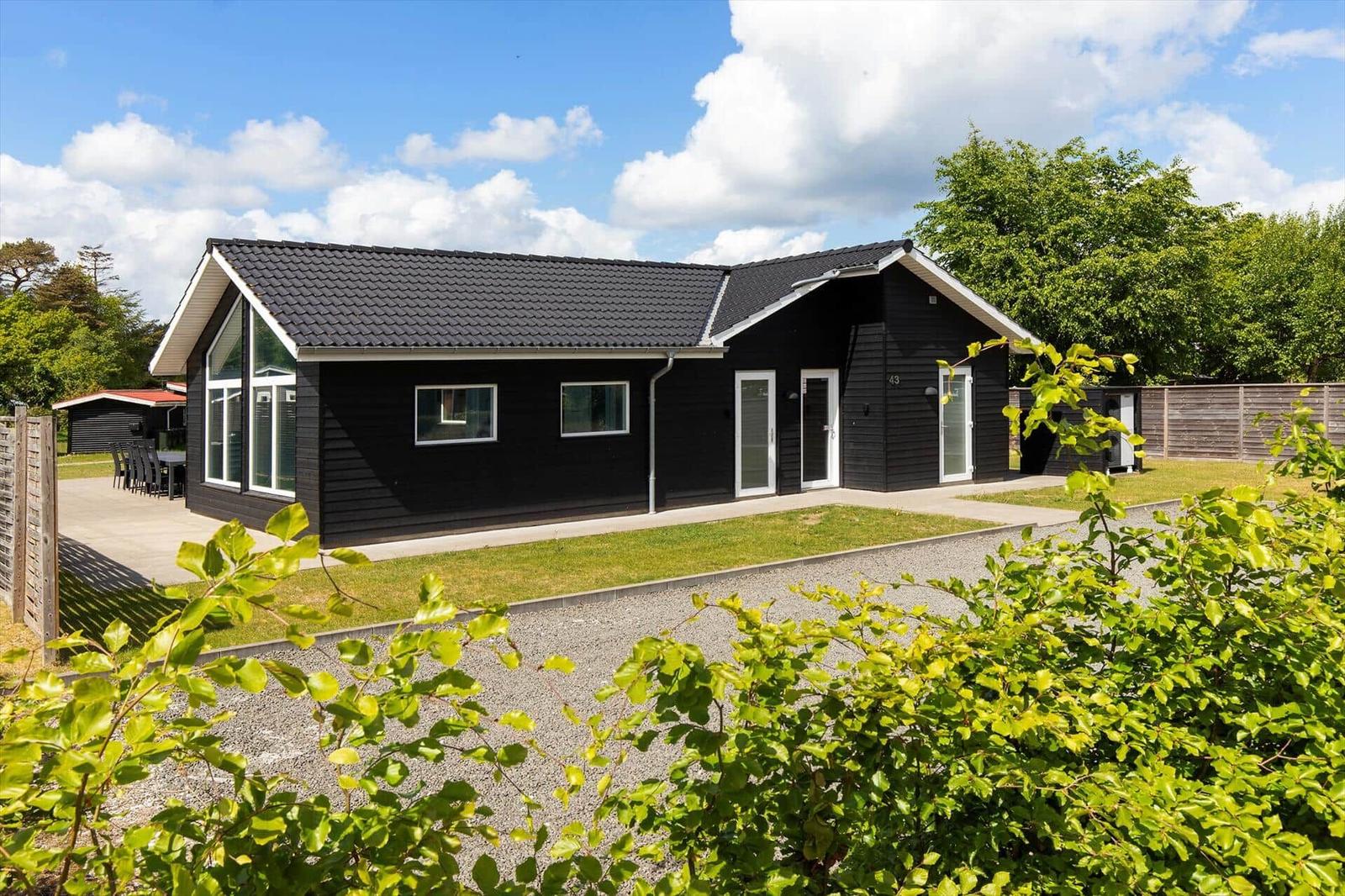 Schwarzes Ferienhaus mit weißem Fensterrahmen und Garten. Hinterhof mit Tisch und Stühlen.