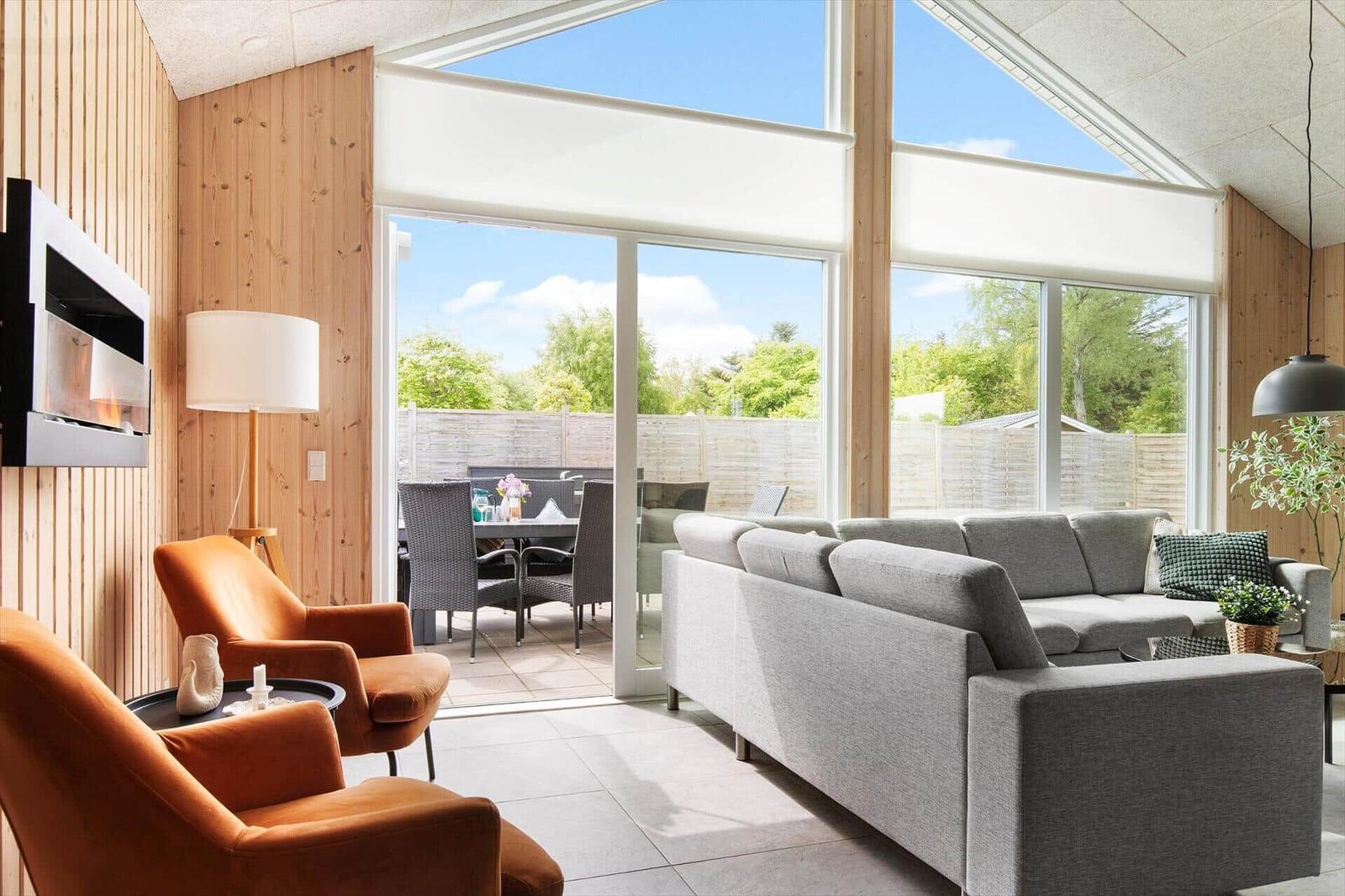 Wohnbereich mit grauem Sofa, orangefarbenen Sesseln und Blick auf den Garten.