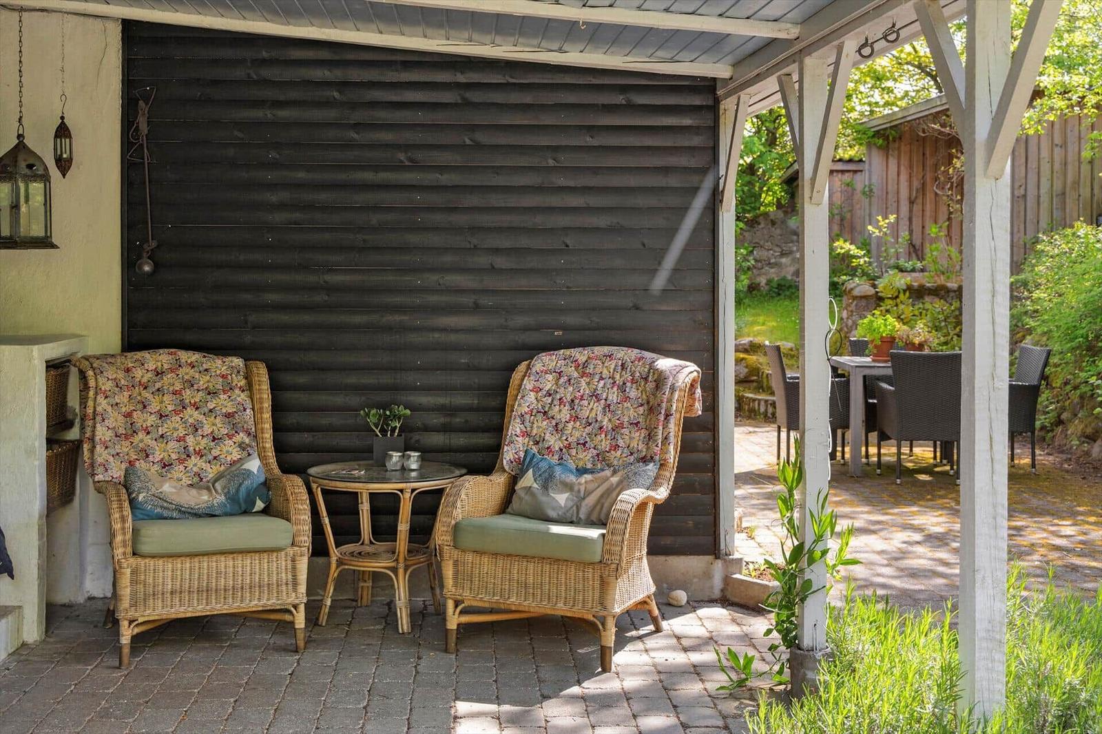 Zwei Stühle mit floralen Bezügen und ein kleiner Tisch stehen unter einer Veranda.