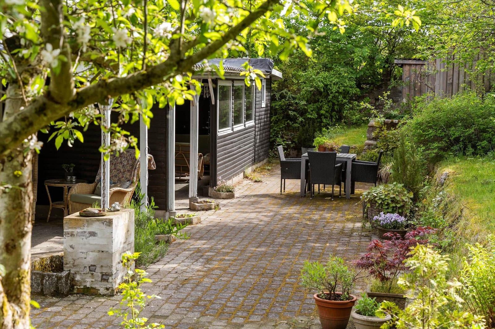 Hinterhof mit Terrasse, Gartenmöbeln und Pflanzen. Schwarzes Holzhaus mit Veranda.