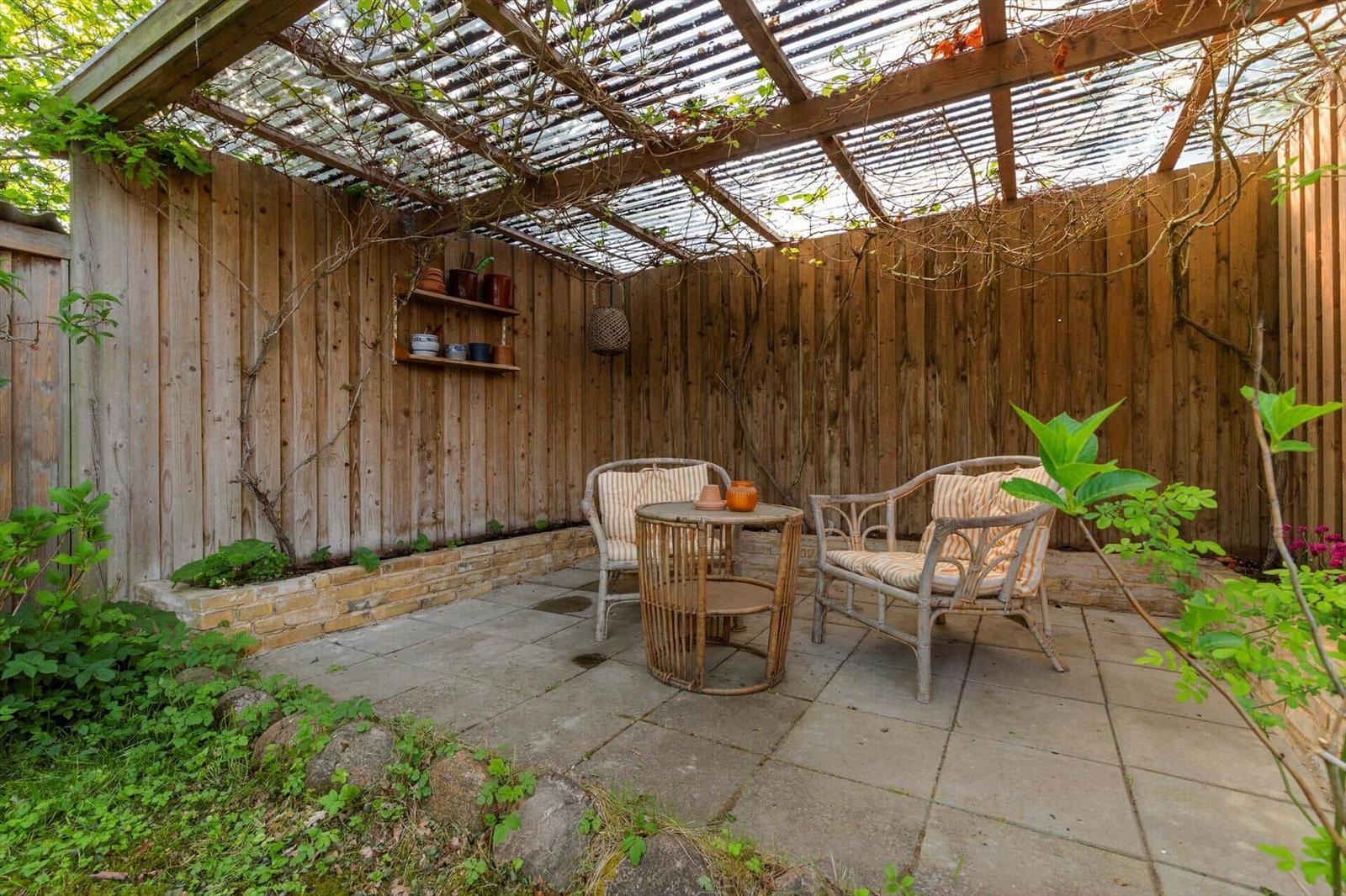 Gartenbereich mit Sitzgelegenheiten unter einem Dach aus Holz und Wellblech.
