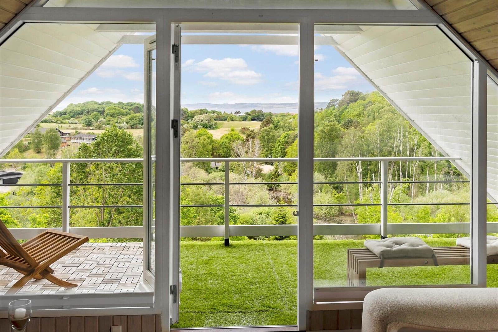 Durch große Fenster blickt man auf einen grünen Garten und Wald.