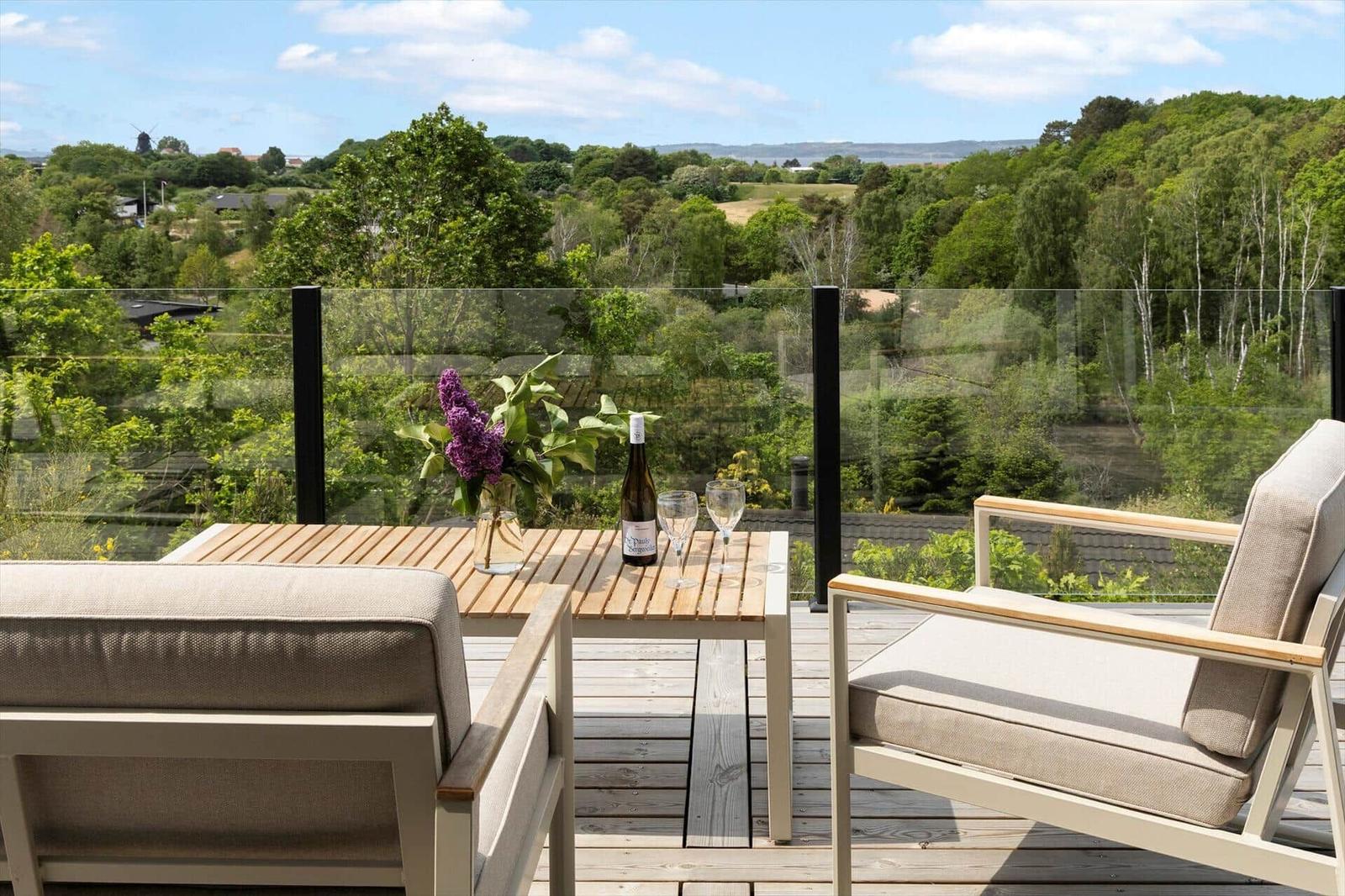 Terrasse mit Tisch, zwei Stühlen, Wein und Lilien. Blick auf grüne Landschaft.