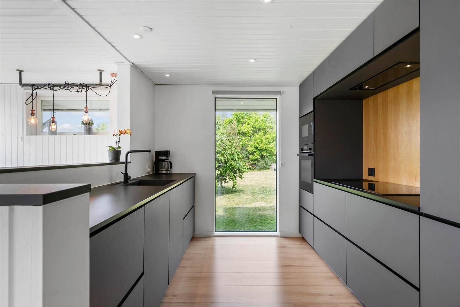 Moderne Küche mit grauen Schränken, Holzboden und Blick auf Garten.