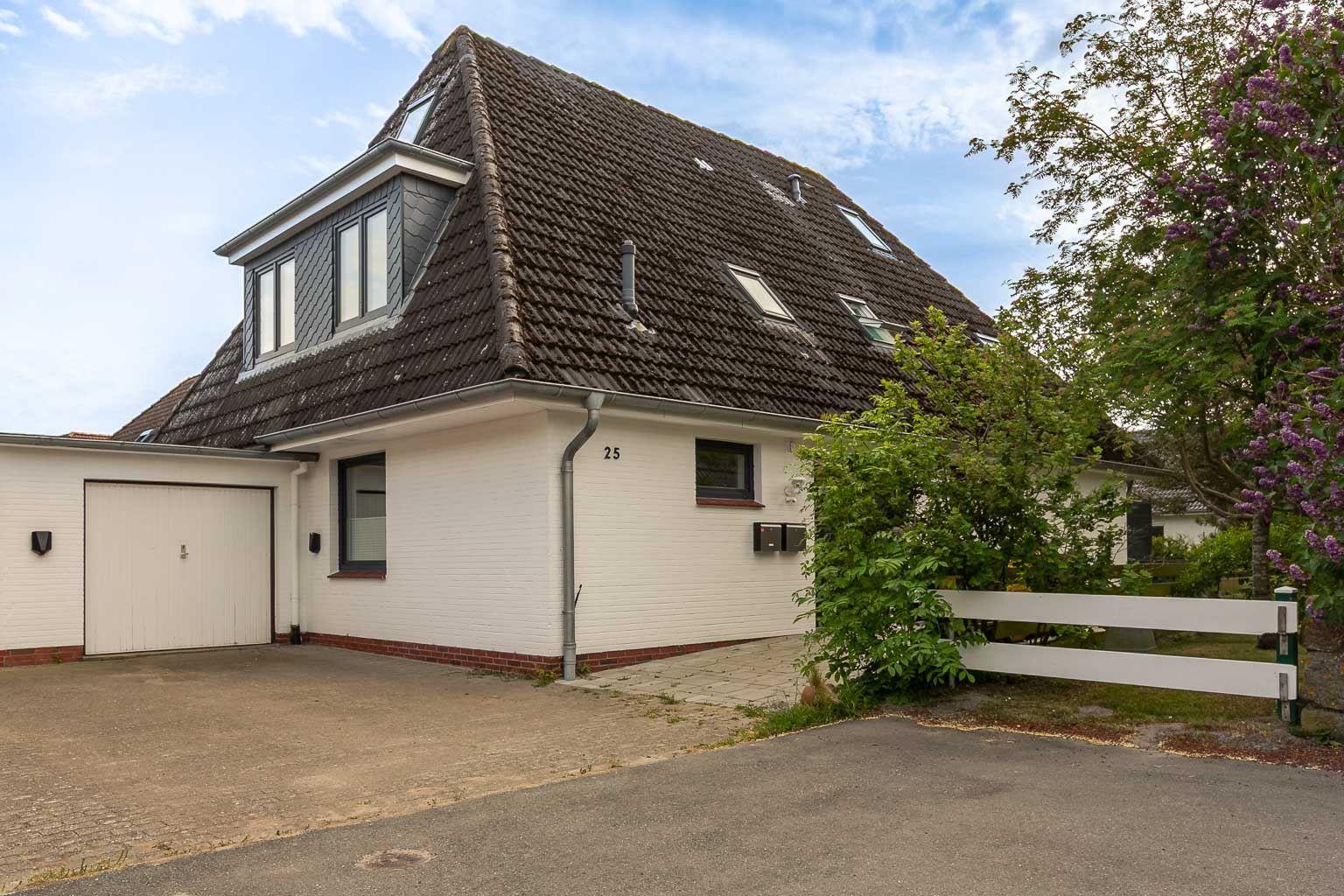 Haus mit dunklem Dach, weißer Fassade und Garage. Umgeben von Grün und einem weißen Zaun.