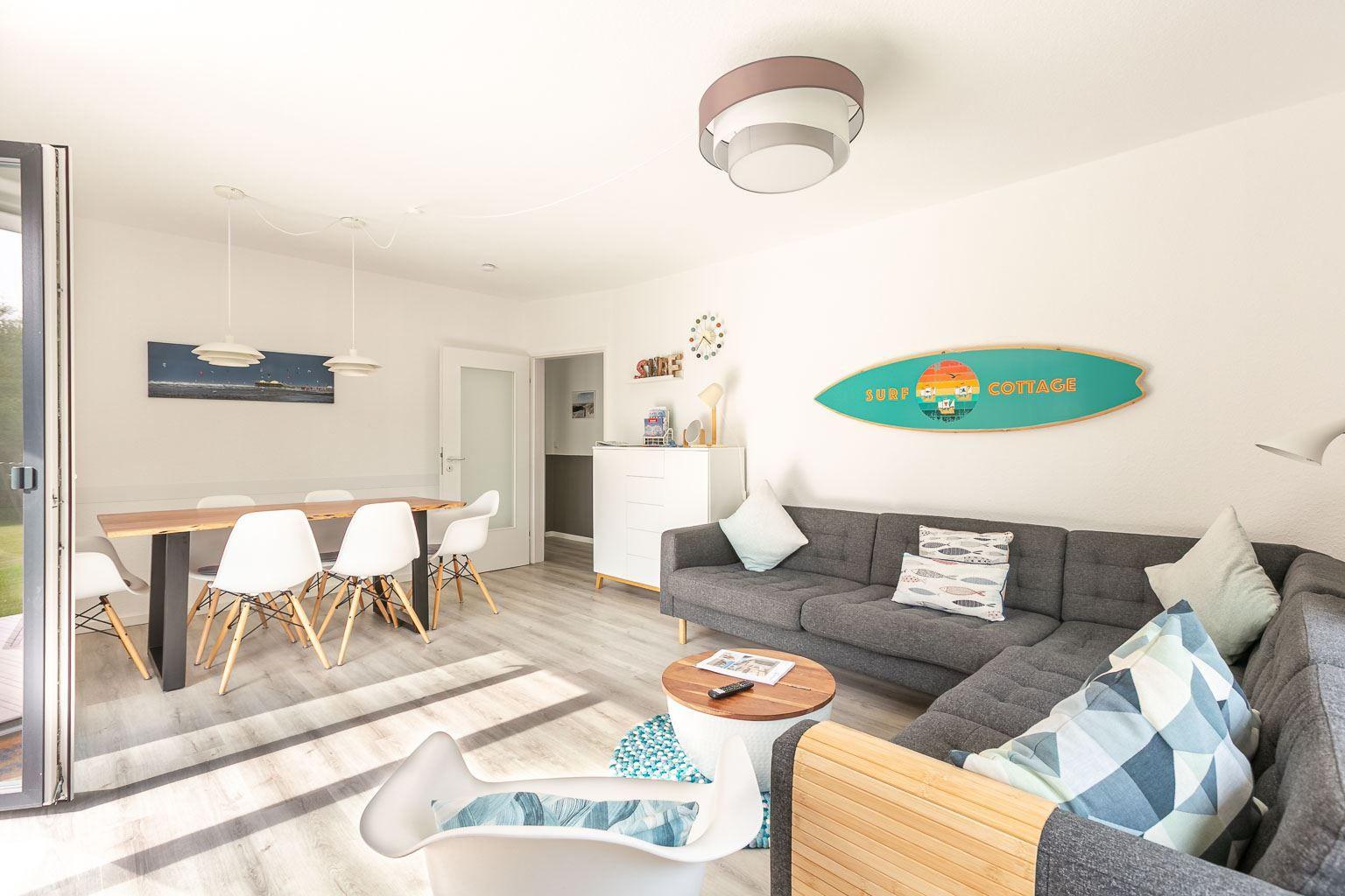 Wohn- und Essbereich mit Sofa, Tisch und Stühlen. Wanddekoration mit Surfboard.