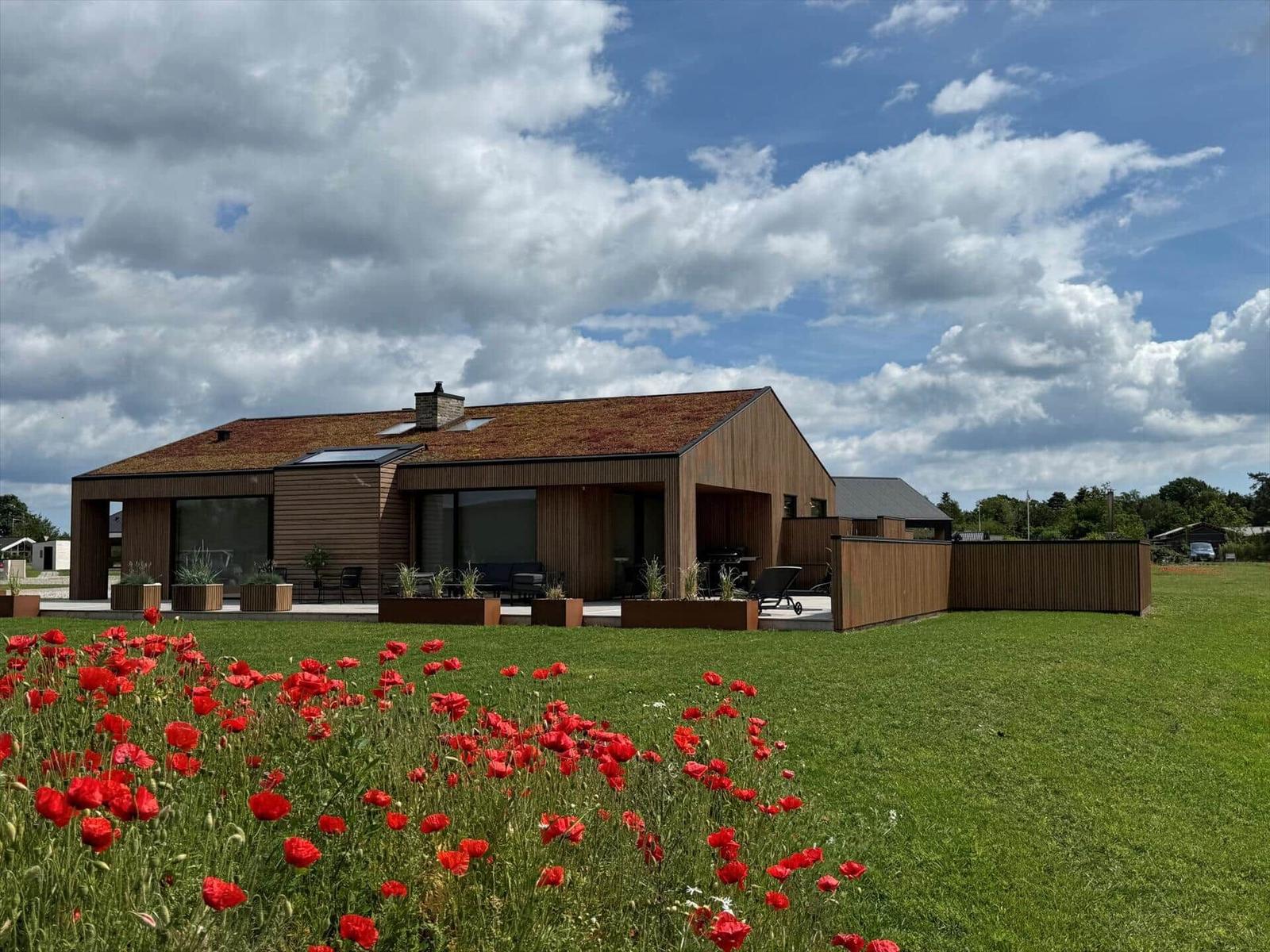 Moderne Holzhäuser mit Terrasse und Blumenfeld im Vordergrund.