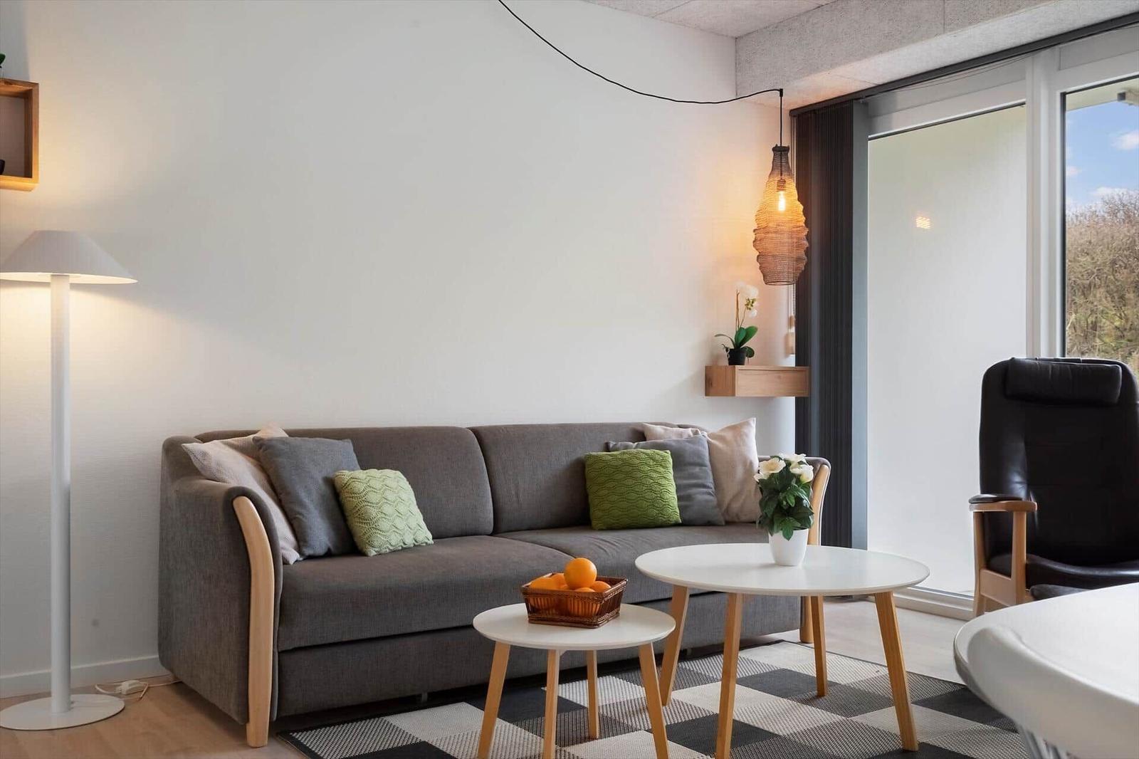 Ein Wohnzimmer mit grauem Sofa, zwei runden Tischen und einer Glastür zum Balkon.
