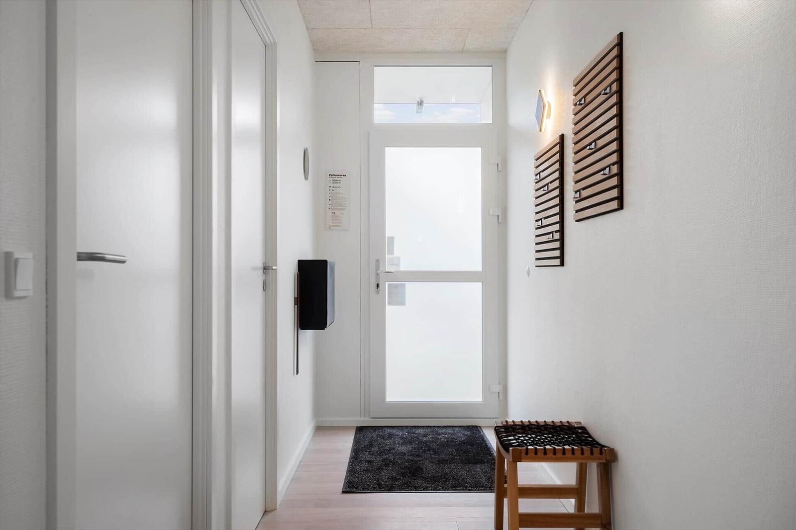 Eingangsbereich mit Tür, Teppich und Holzstuhl an der Wand.