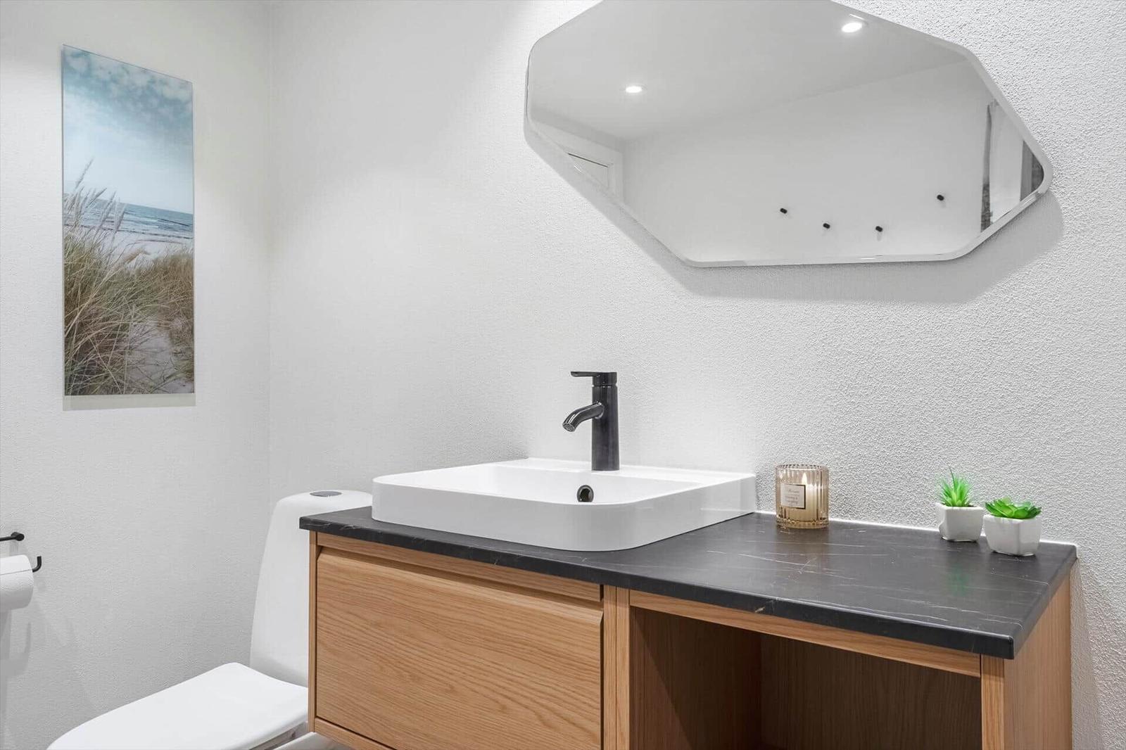 Badezimmer mit Waschbecken, Spiegel und Toilette. Wandbild und Pflanzen auf der Arbeitsplatte.