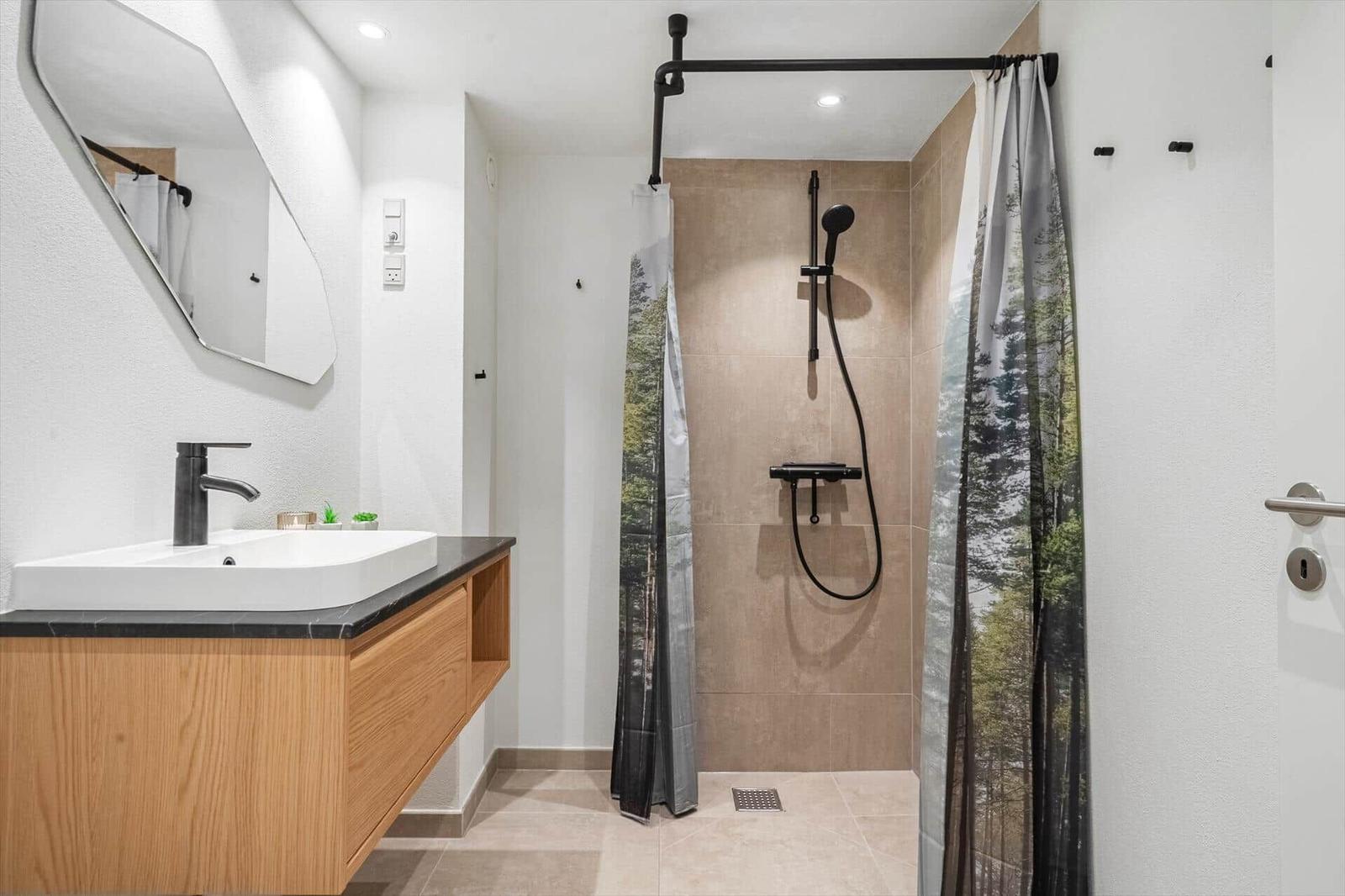 Badezimmer mit Dusche und Waschtisch. Duschvorhang zeigt Waldmotiv.