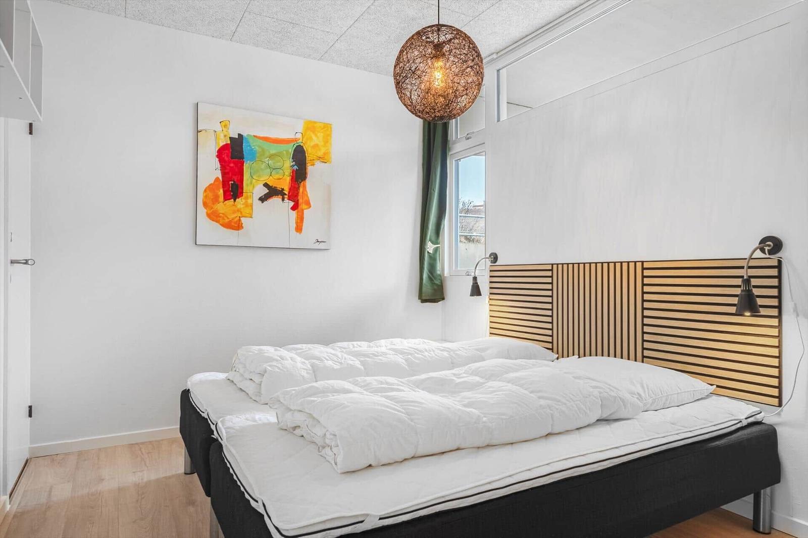 Schlafzimmer mit Bett, Wandbild und Deckenleuchte.