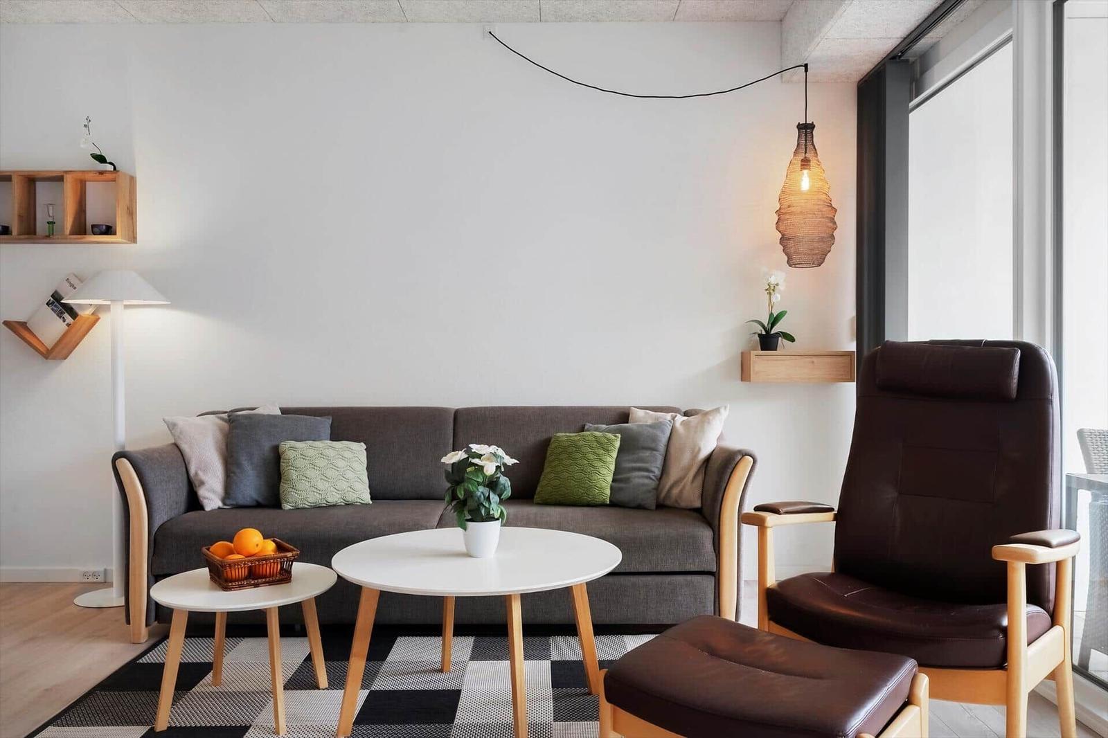 Ein Wohnzimmer mit grauem Sofa, braunem Sessel und runden Tischen.