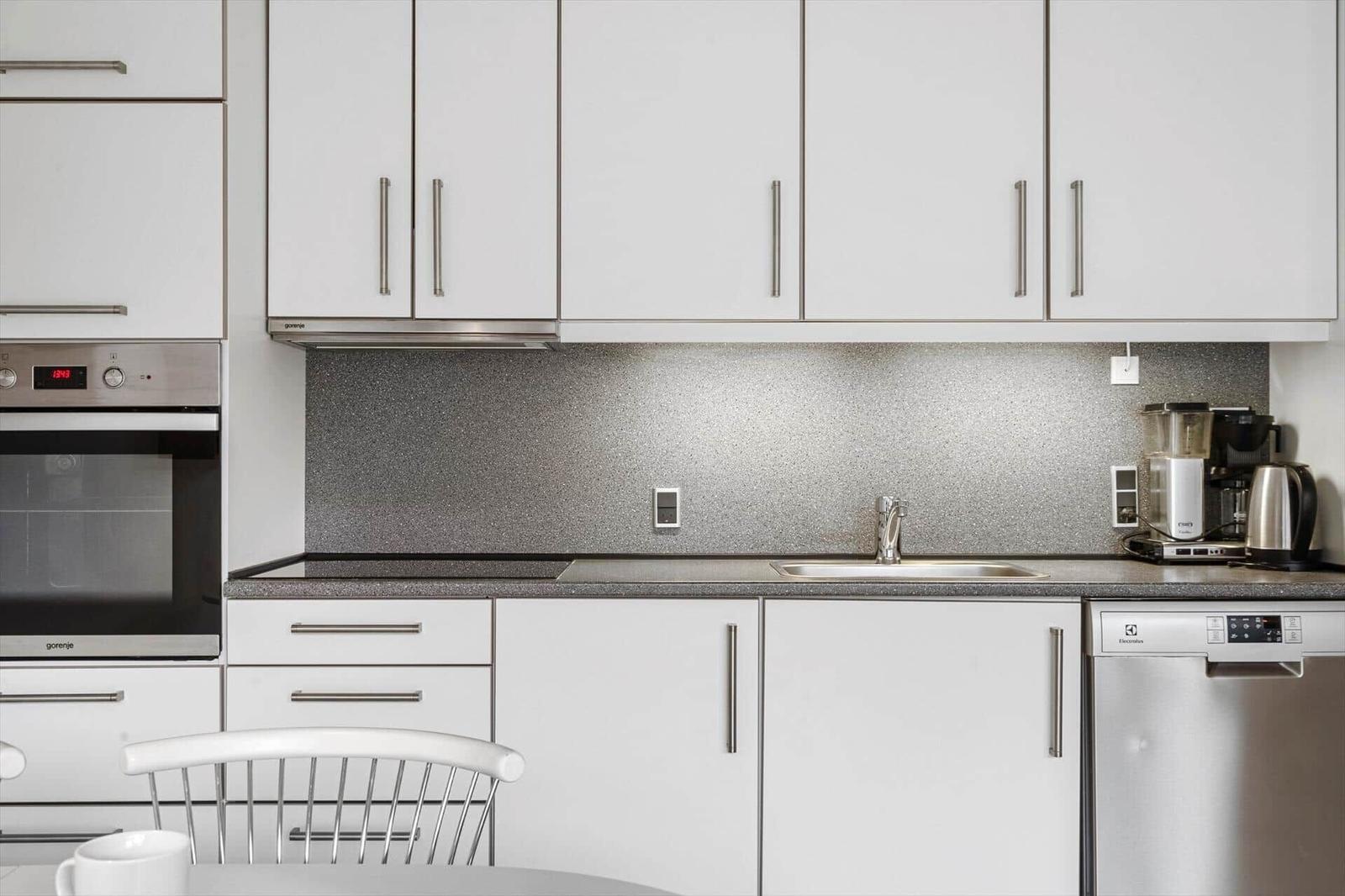 Moderne Küche mit weißen Schränken, Edelstahlgeräten und grauem Arbeitsplatz.