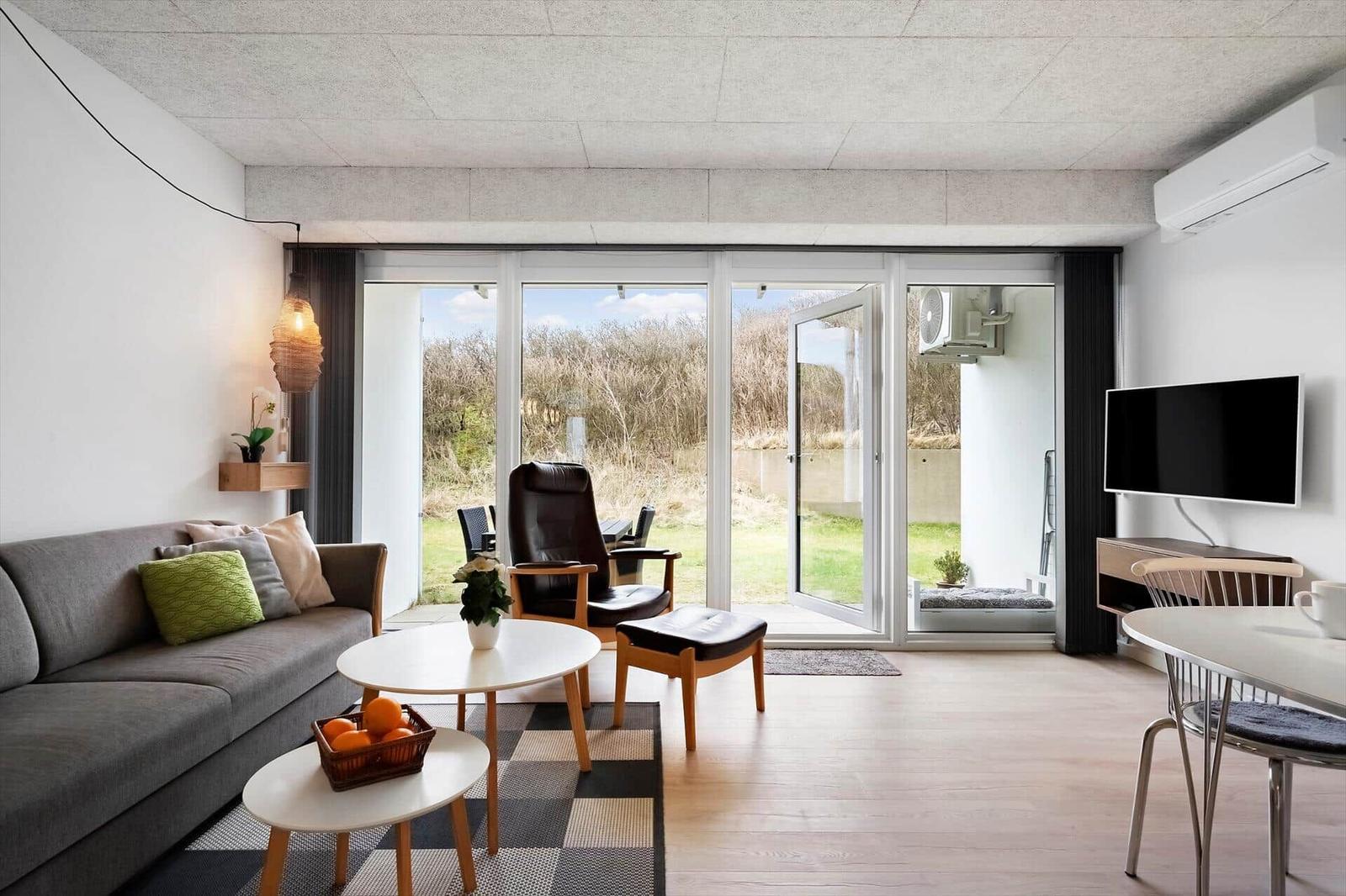 Wohnzimmer mit Sofa, Sitzgruppe und TV. Durchgang zur Terrasse mit Blick auf Grünfläche.