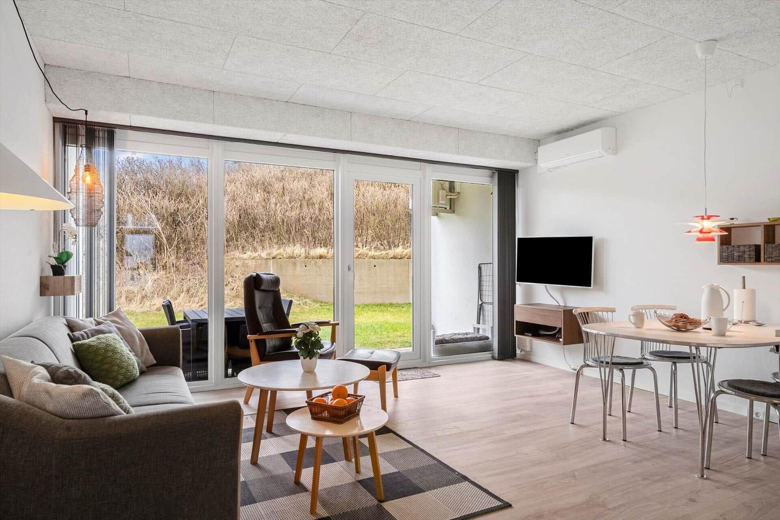 Wohn- und Essbereich mit großem Fenster, Sofa, Tisch und TV.