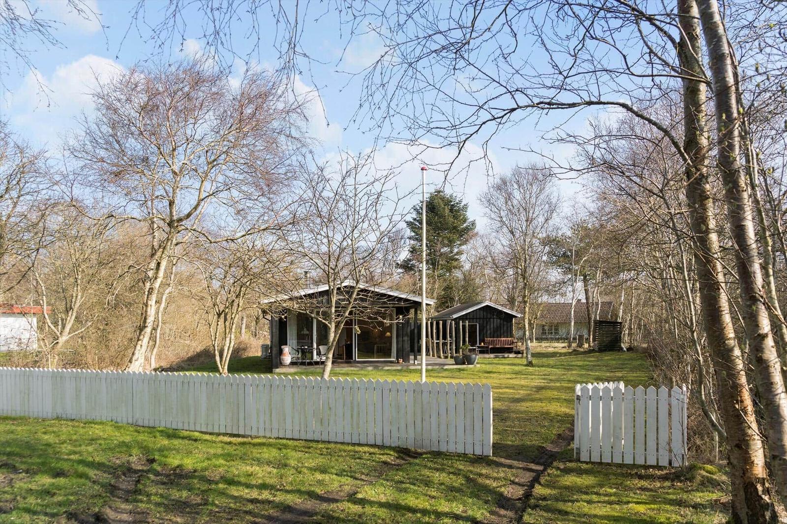 Two wooden houses with terraces stand in a green garden surrounded by trees.