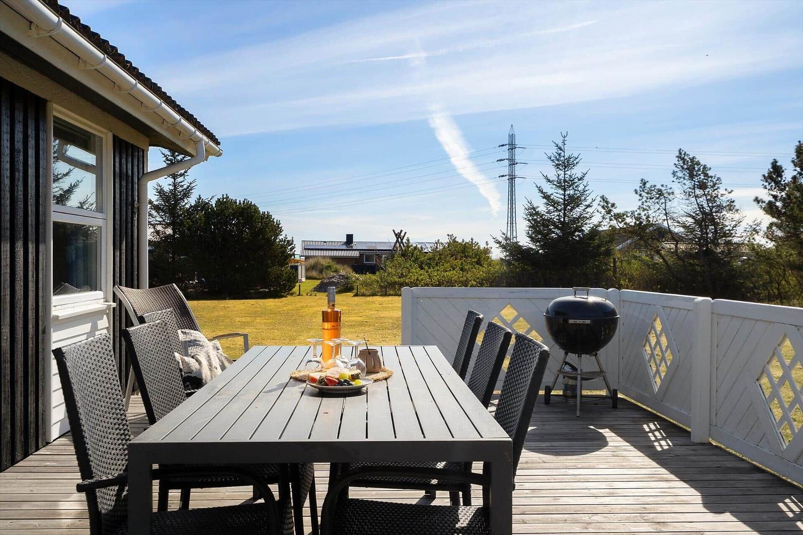 Terrasse mit Tisch, Stühlen und Grill. Blick auf Grasfläche und Bäume.