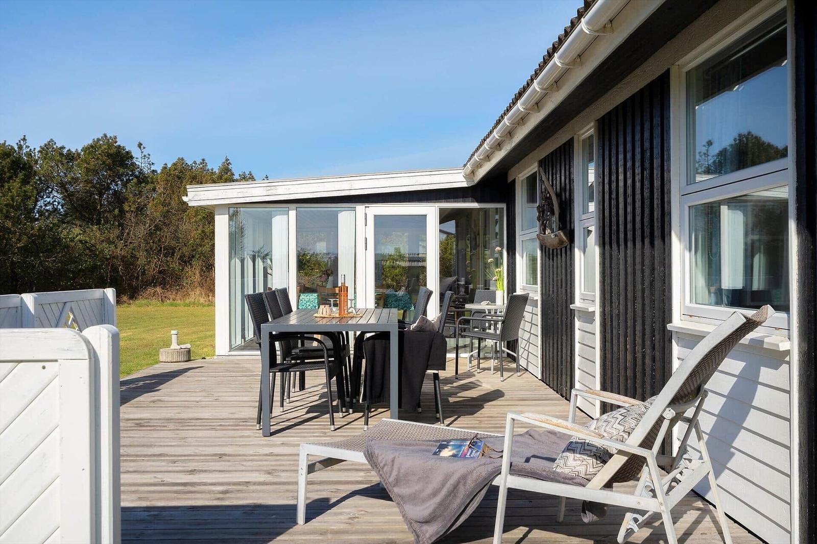 Terrasse mit Tisch, Stühlen und Liegestuhl. Blick auf Garten und Haus.